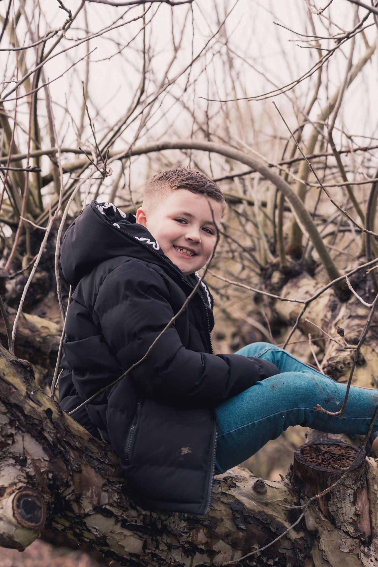 Child in black winter coat climbing tree branches and smiling.