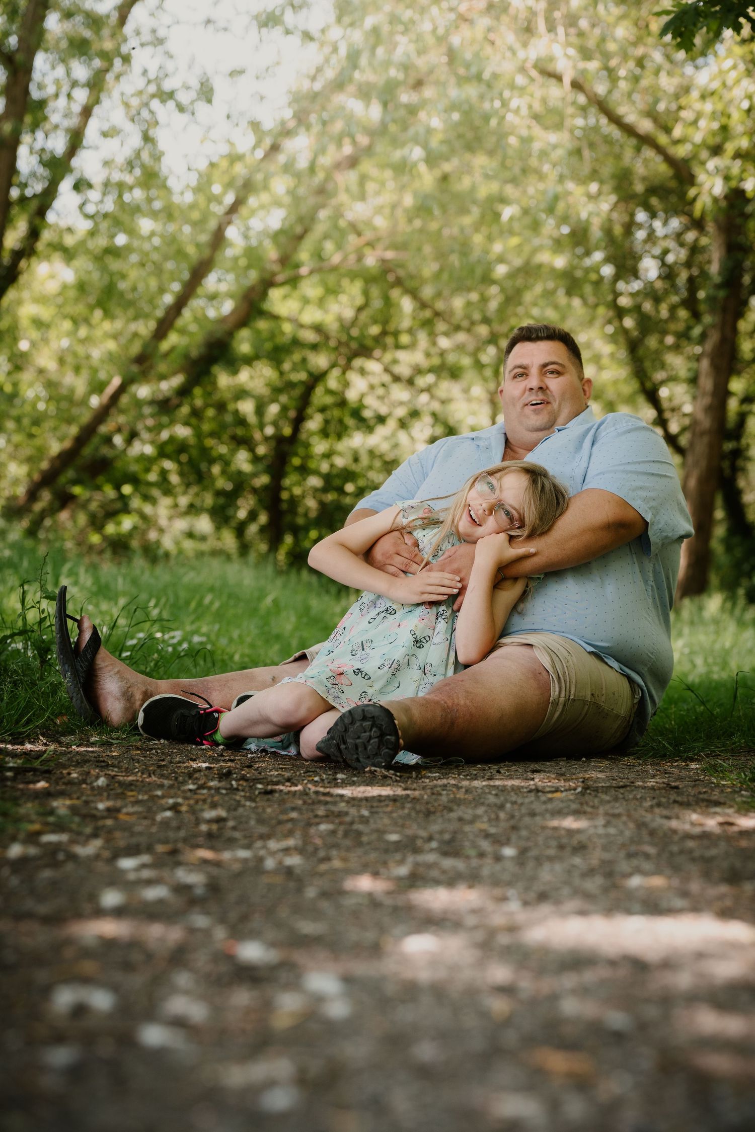 Two people relaxing together on a path surrounded by green trees.