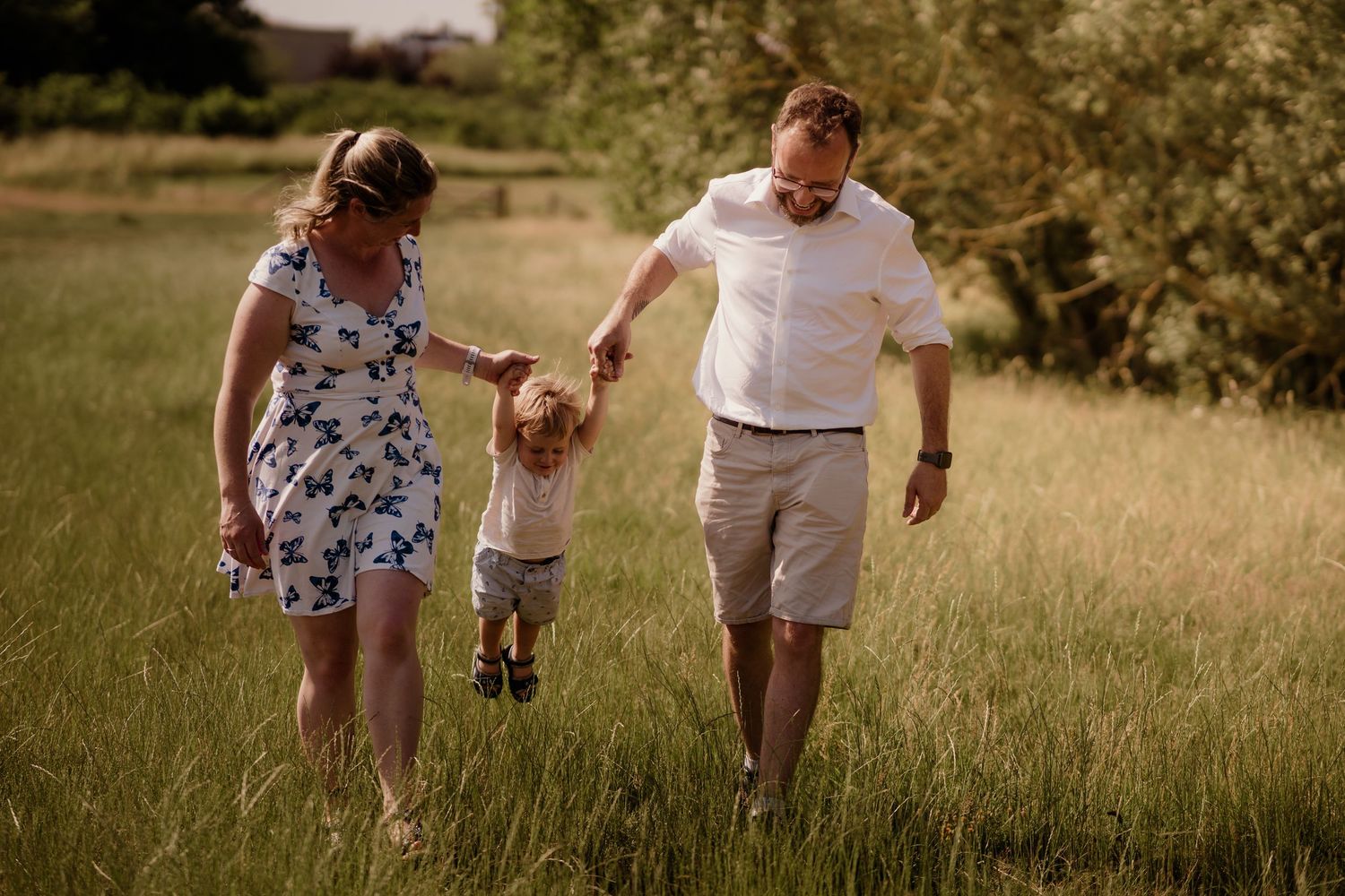 Family walking together through tall grass in summer field.