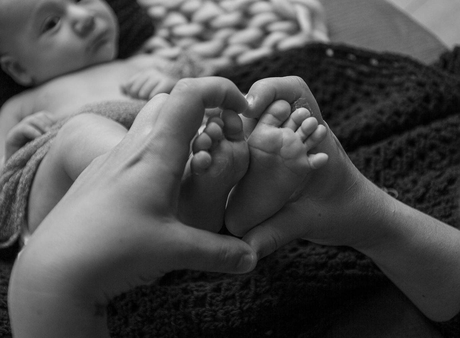 Black and white image of tiny baby feet being held by adult hands.
