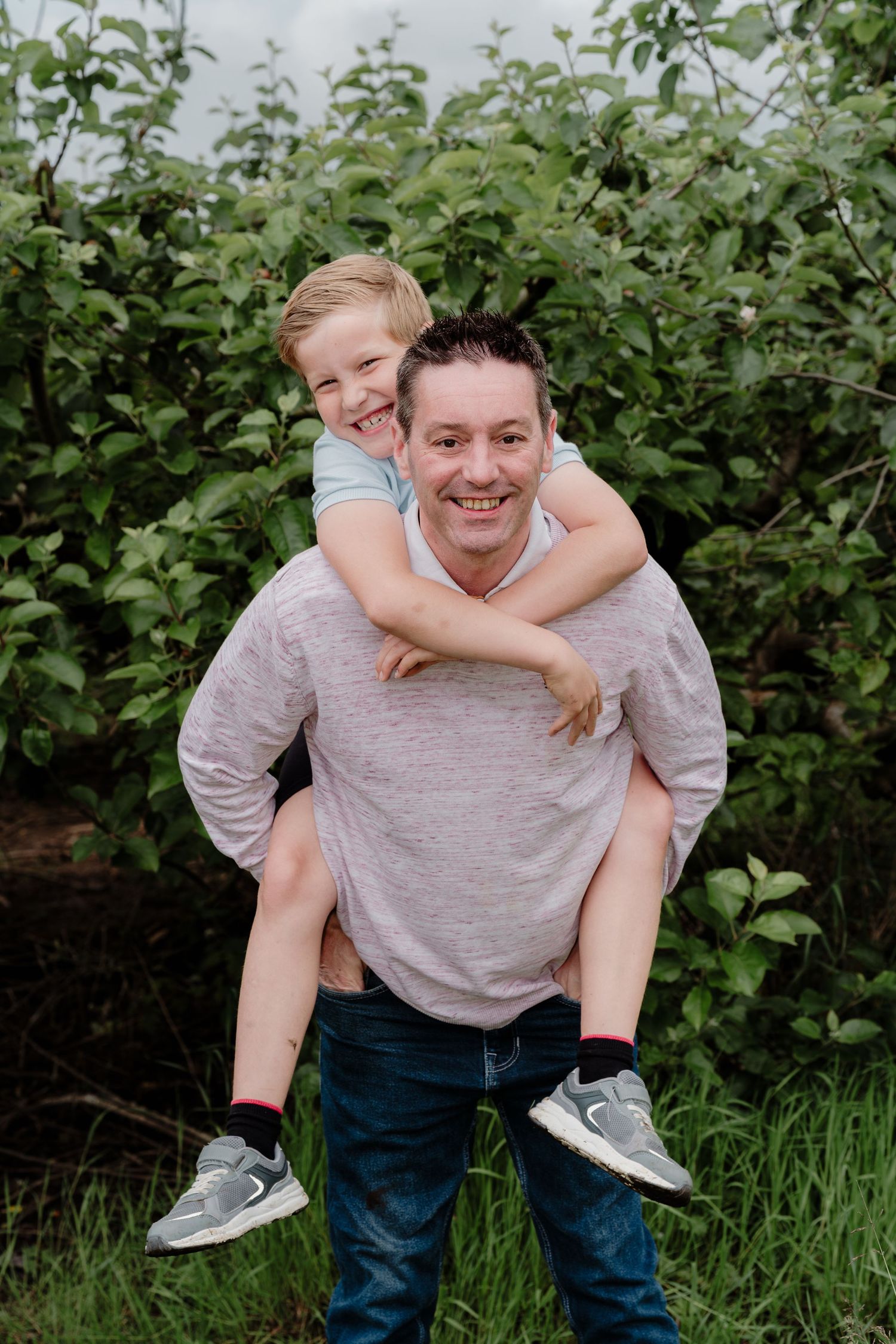 Playful piggyback ride moment captured in front of green foliage.