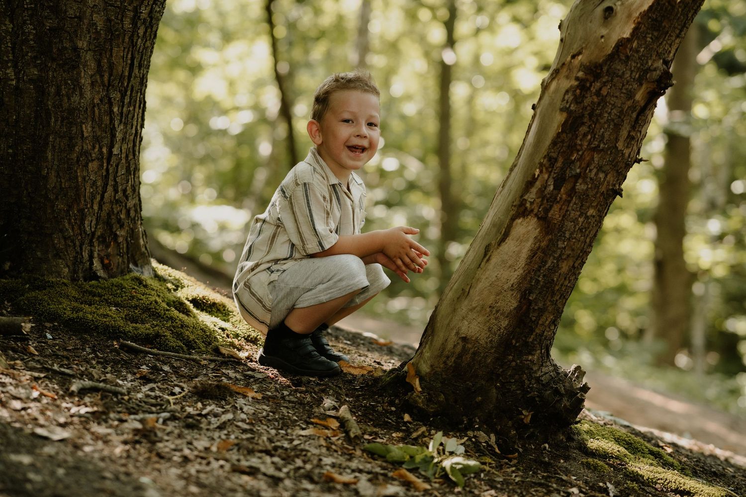 Child crouching by a tree trunk in a magical forest setting with natural sunlight.