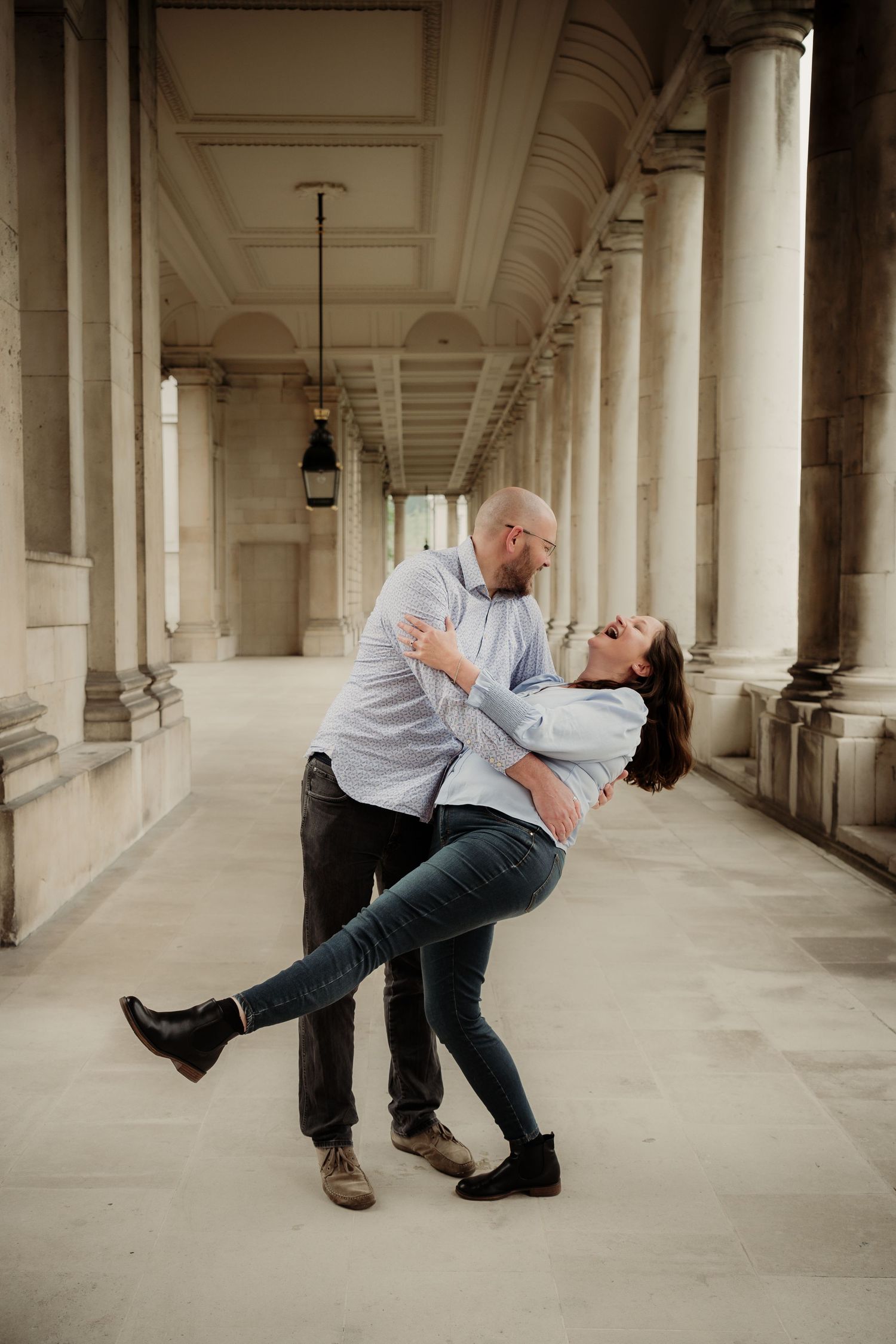 A couple performing a romantic dip pose in an elegant columned hallway.