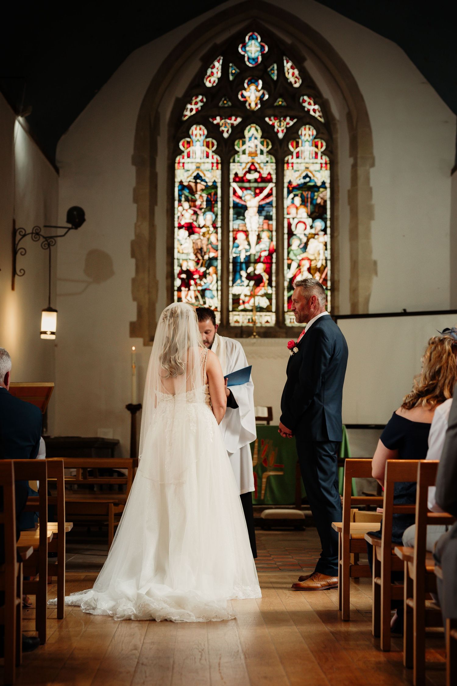 Wedding ceremony in a church with beautiful stained glass windows and wooden pews.