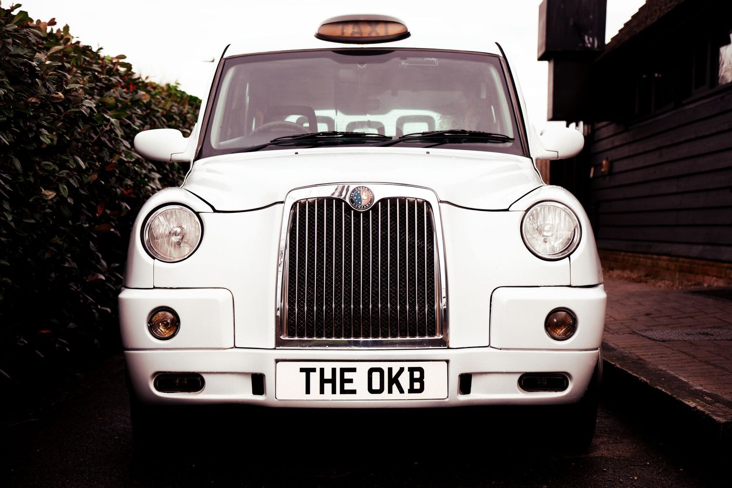 A classic white London taxi cab with 'THE OKB' license plate parked on a street.
