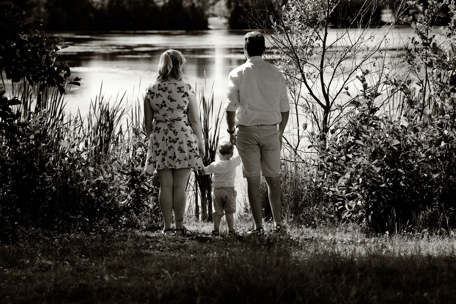Family standing together by lake at sunset in black and white.
