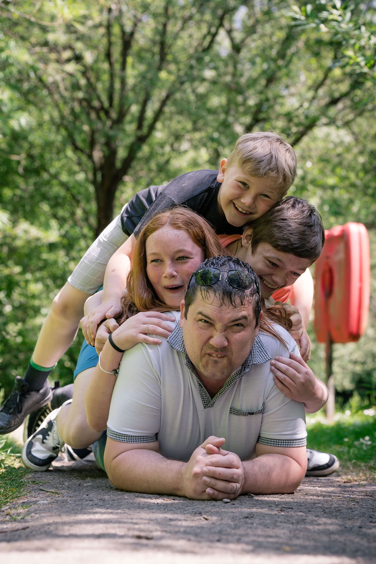 A playful family pile laying on a wooden deck surrounded by green trees.
