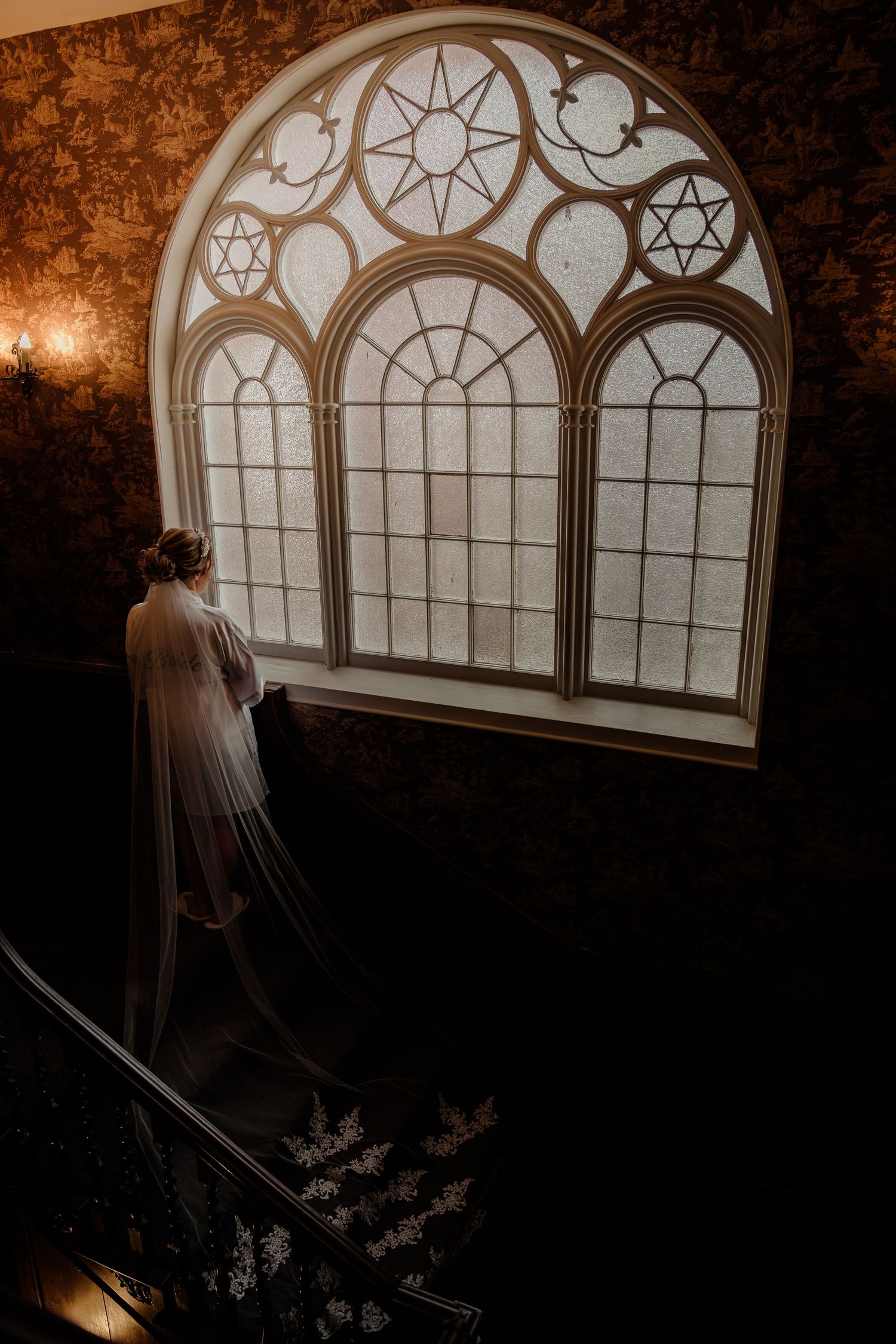 A silhouette of a bride standing by an ornate arched window with decorative geometric patterns.