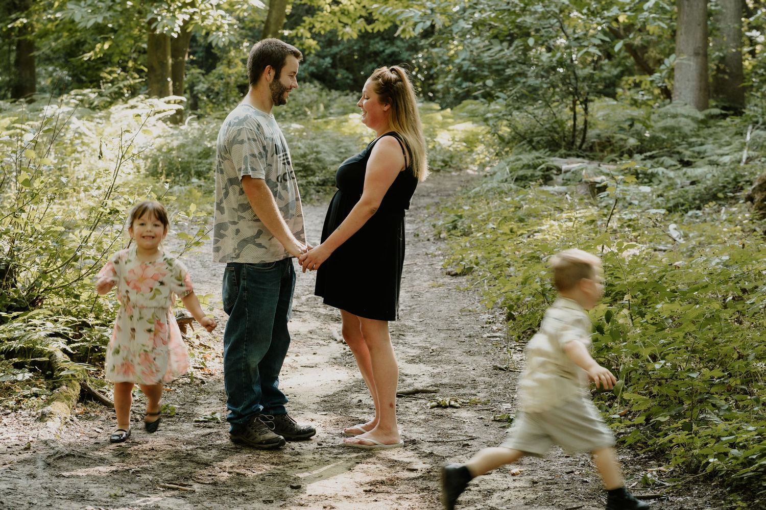 Family walking together on a forest path with children playing in summer sunlight.