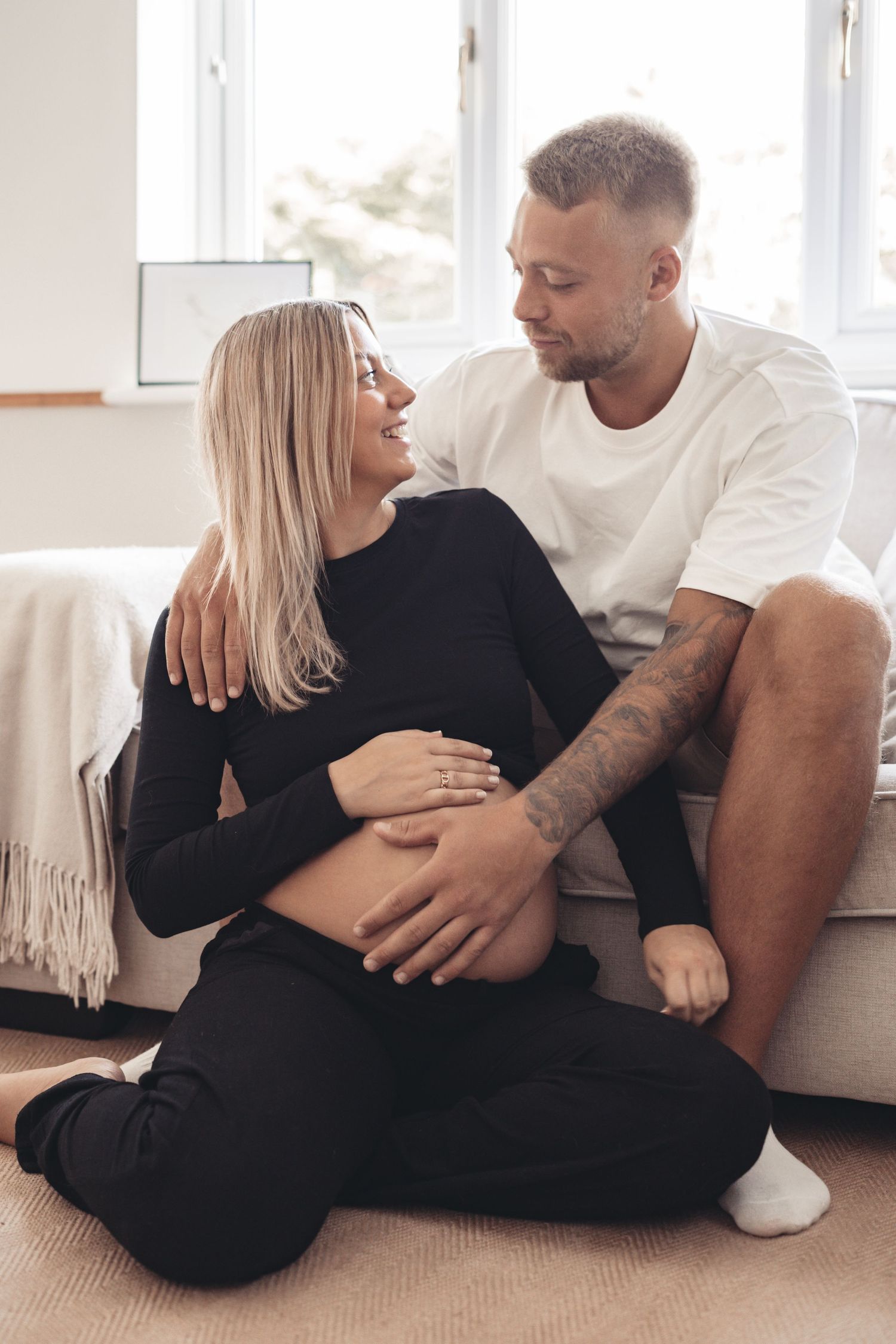Intimate maternity photoshoot showing couple cuddling on white couch.