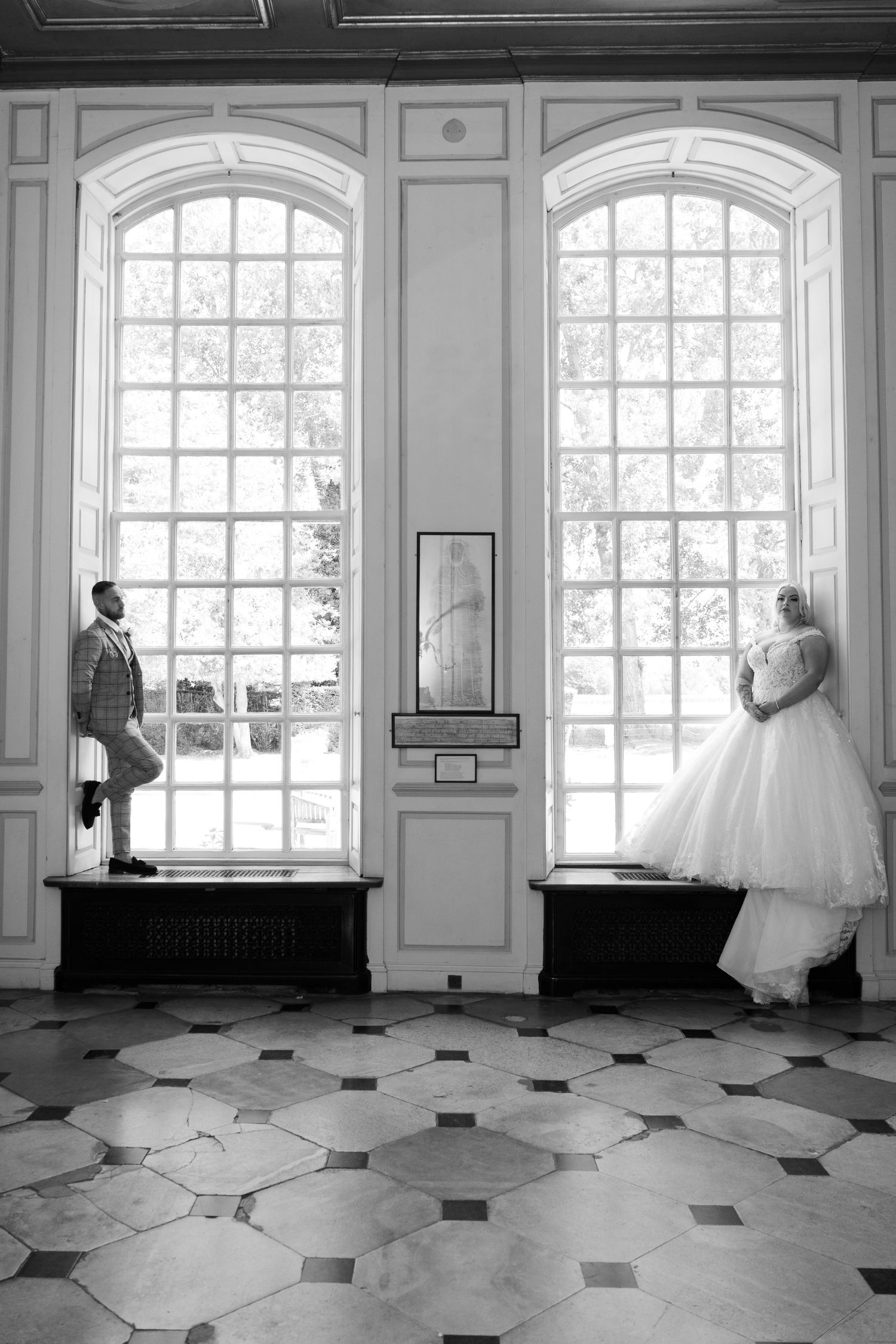 A creative wedding photo with couple standing in separate arched windows with geometric floor pattern.