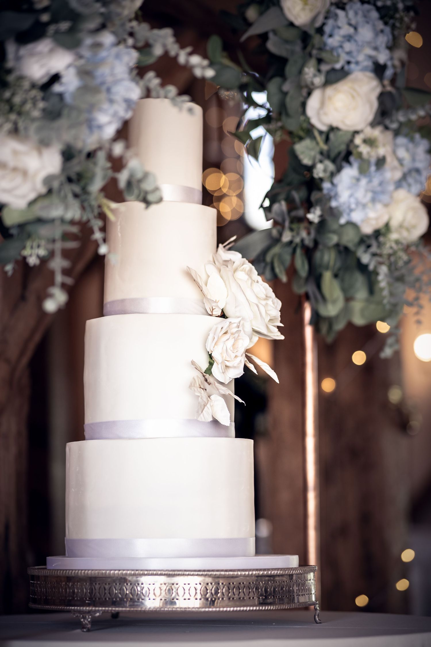 Elegant white tiered wedding cake decorated with light blue flowers and silver accents.
