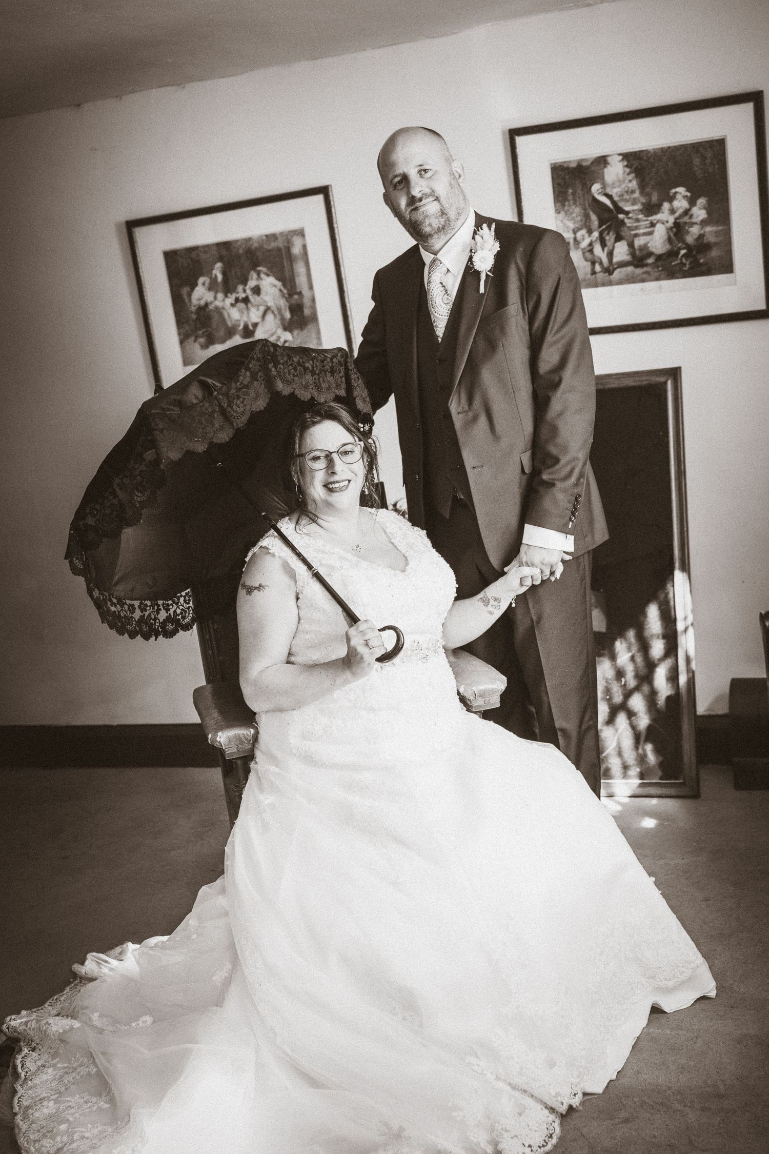 A couple poses together with a vintage parasol in a formal black and white portrait.