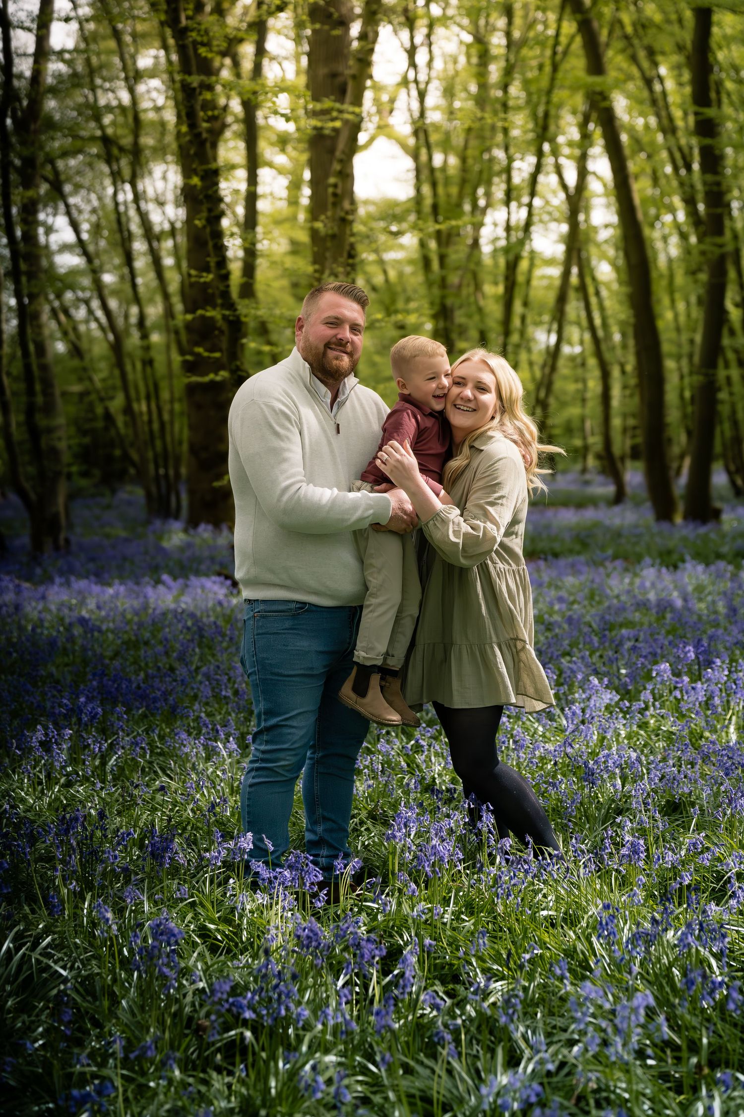 Family embracing and laughing together in a magical bluebell woodland setting.