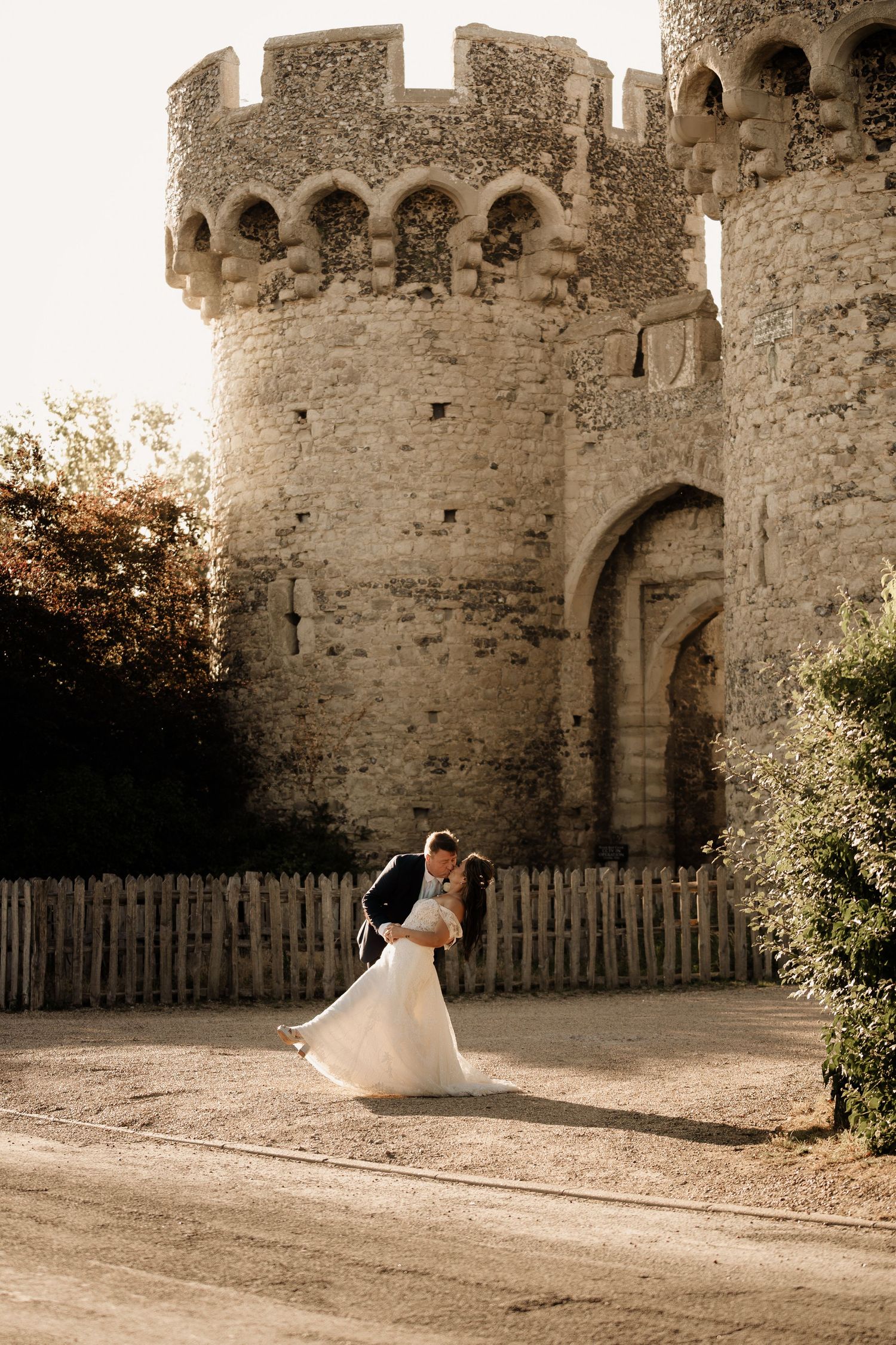 Newlyweds share romantic moment in front of ancient stone castle wall.