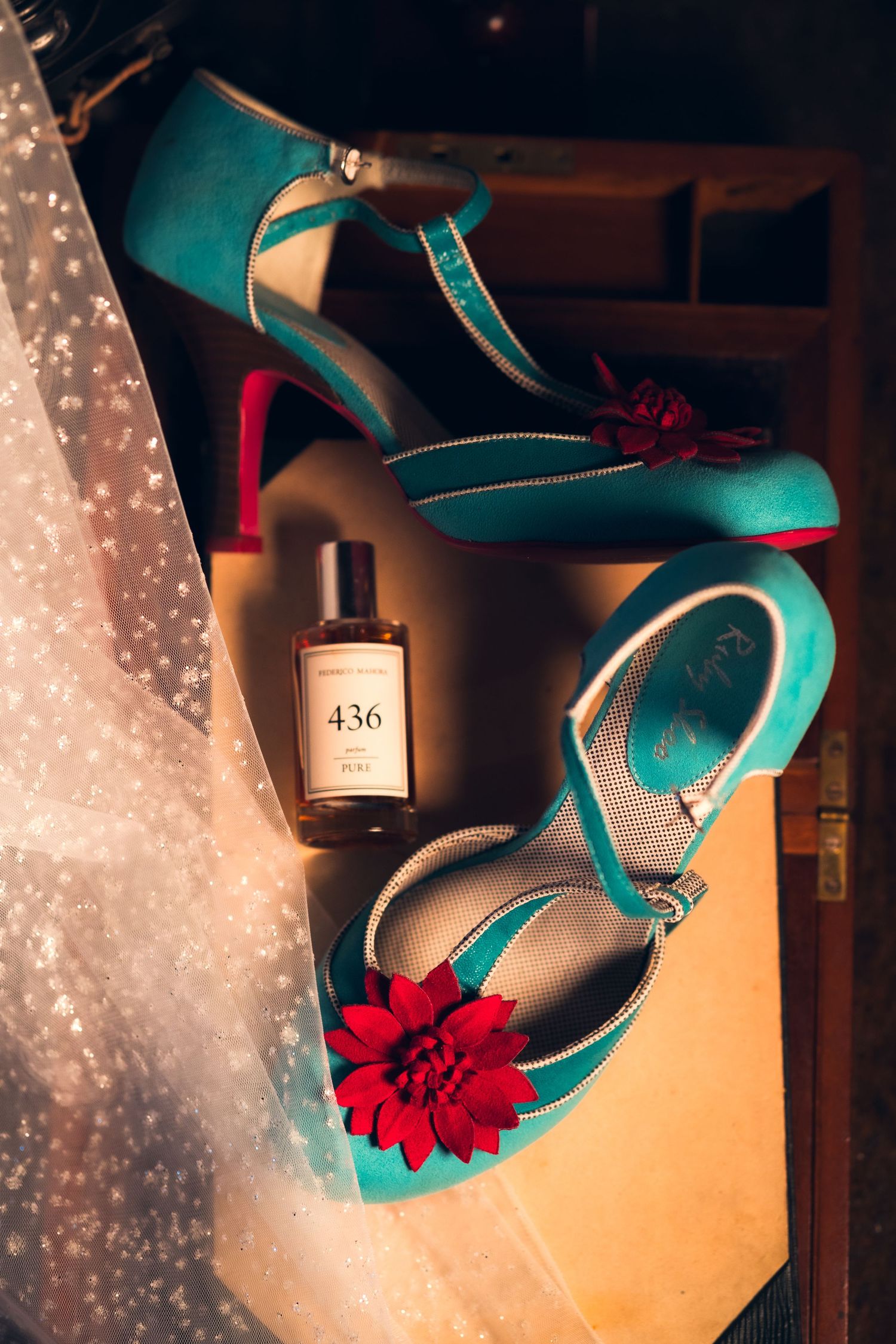 Teal wedding shoes with red flower accents displayed against a glowing backdrop.