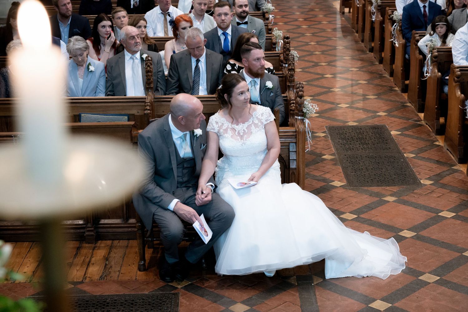 A wedding couple seated in a traditional church with brick walls and wooden pews during their ceremony.