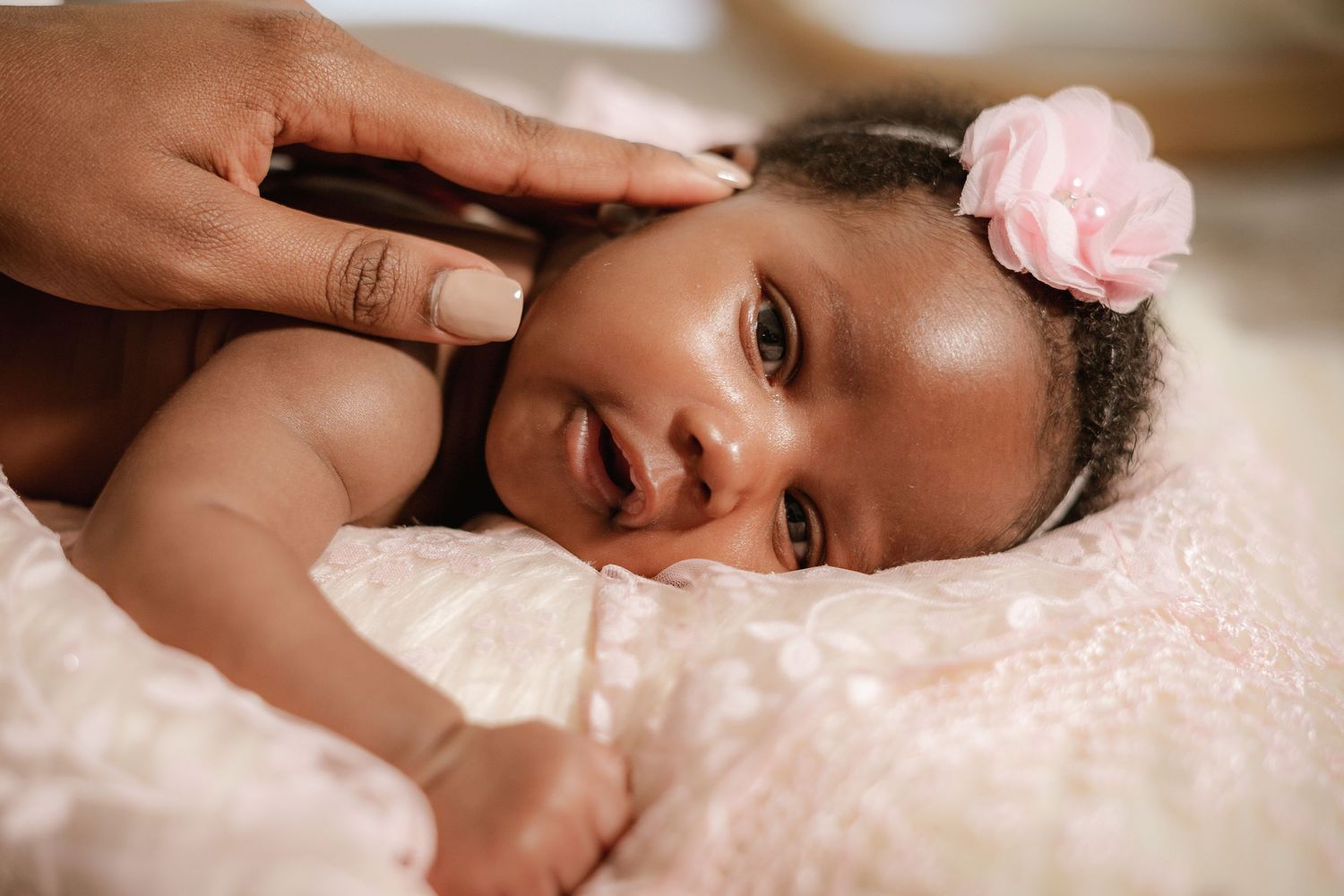 Close-up portrait of baby with pink flower accessory on soft bedding.
