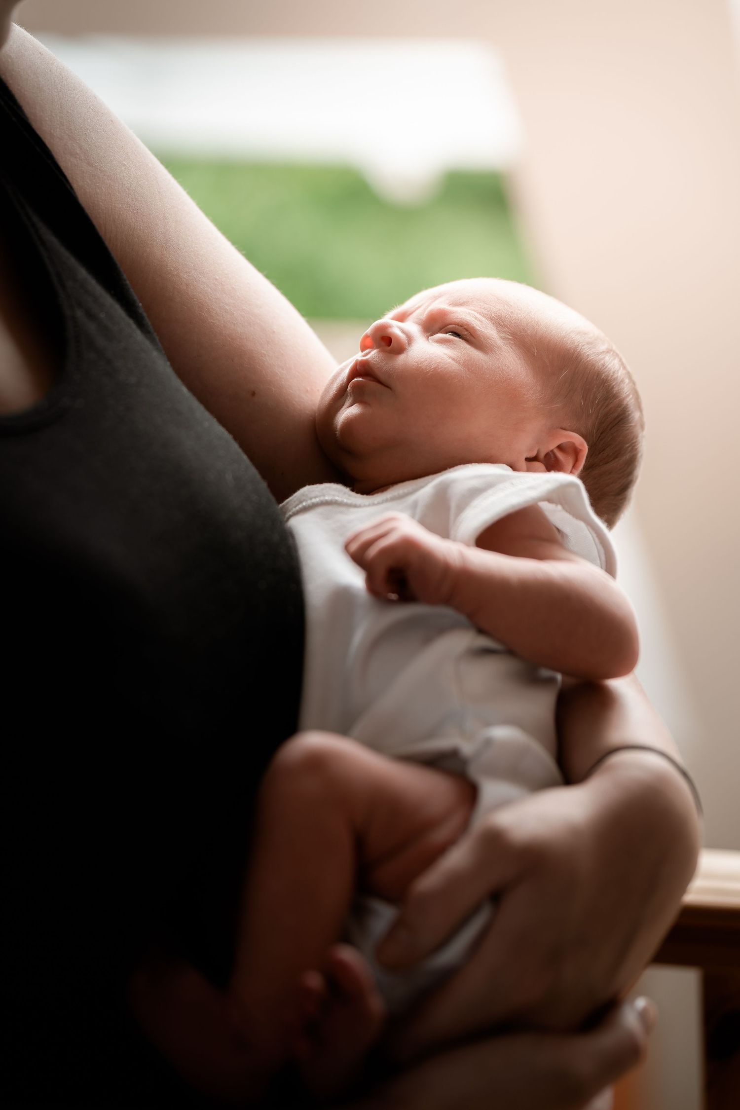 A newborn baby in a white onesie rests peacefully against someone wearing black.