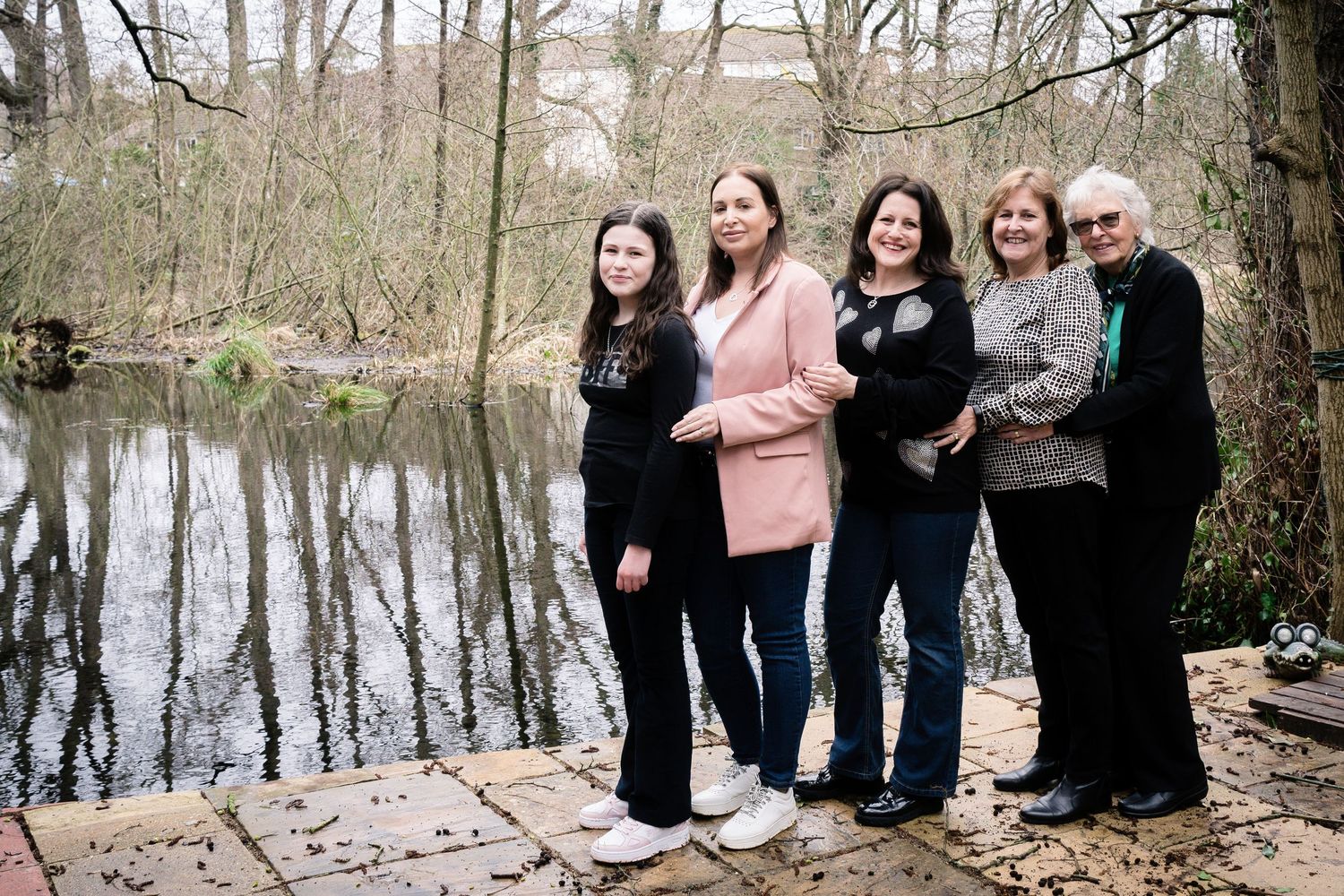 Multi-generational group standing together by a serene pond on a wooden deck.