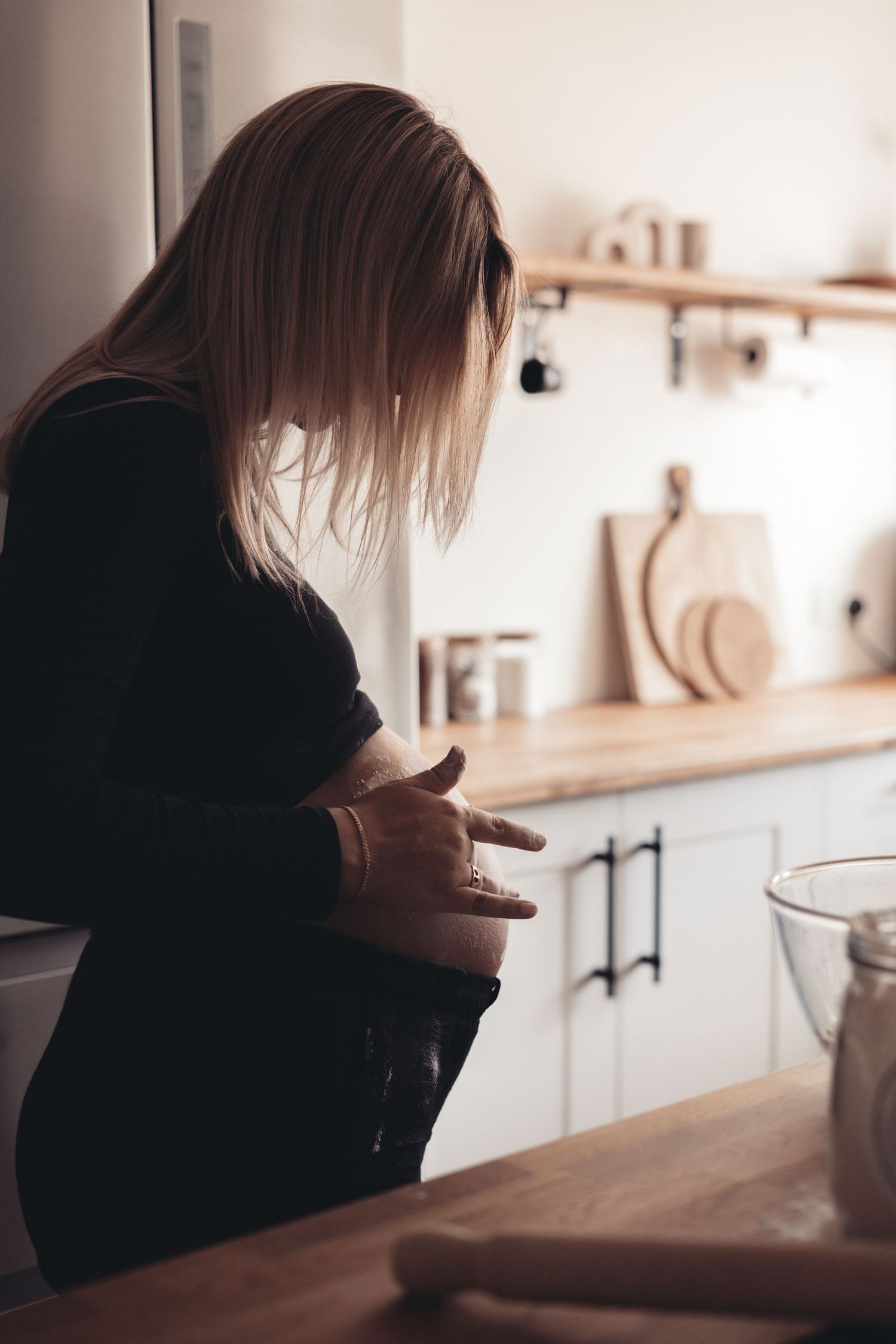 Side profile of expecting mother in black sweater standing in modern kitchen.