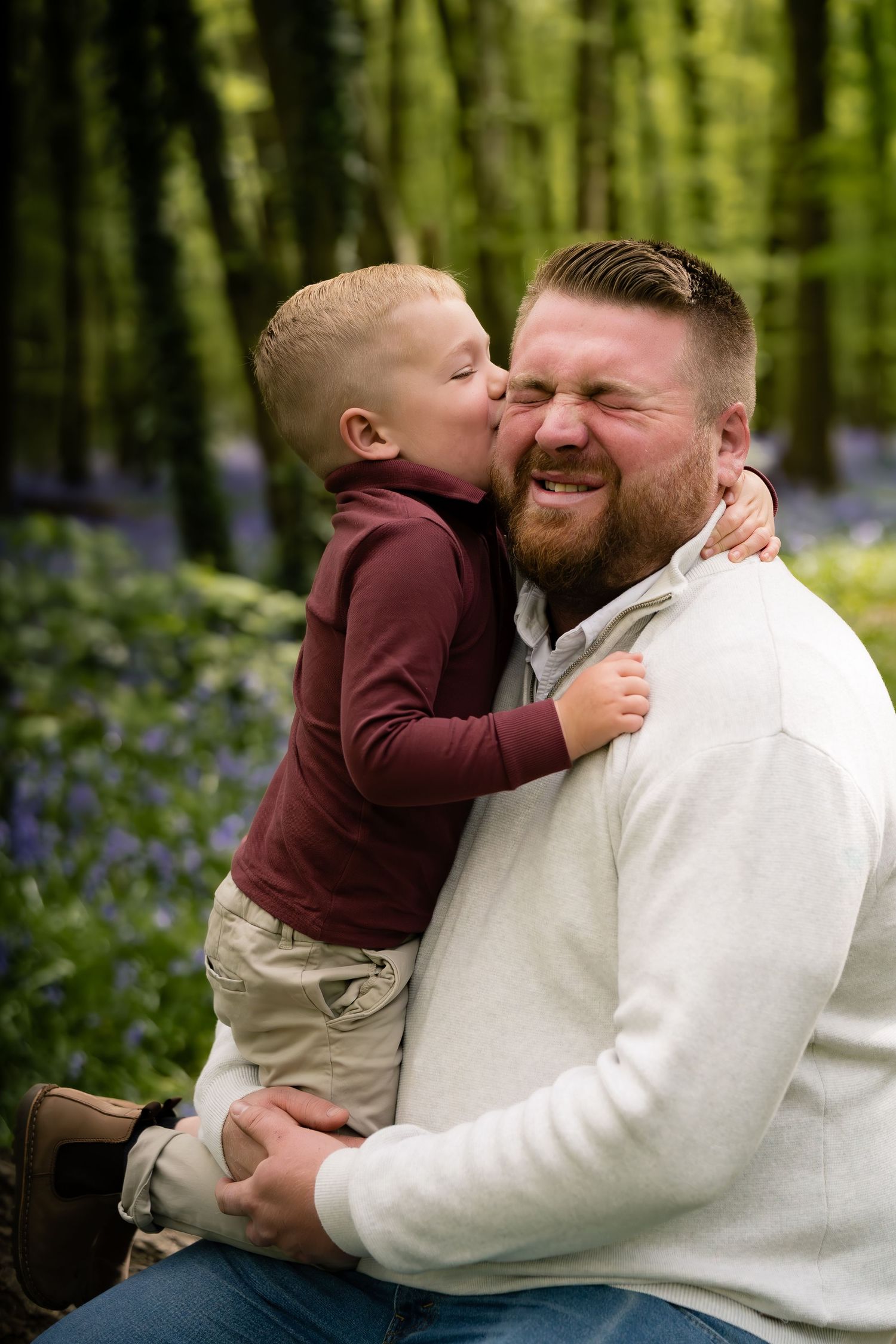 Intimate moment between parent and child sharing affection in a bluebell forest.