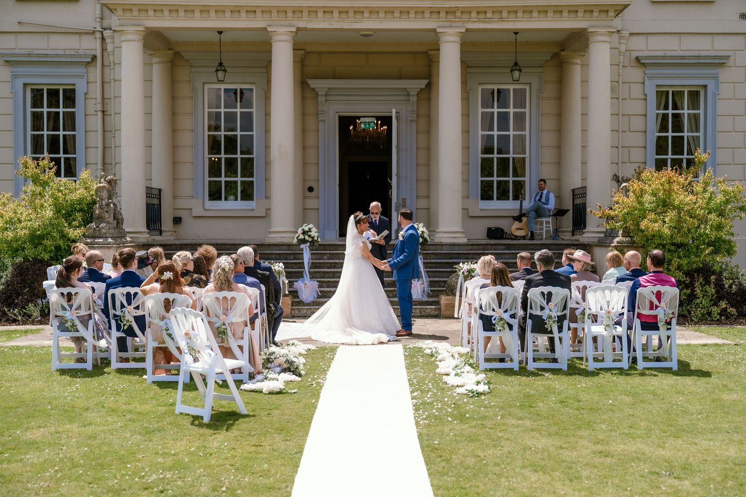 Outdoor wedding ceremony setup with white chairs in front of a stately manor house.