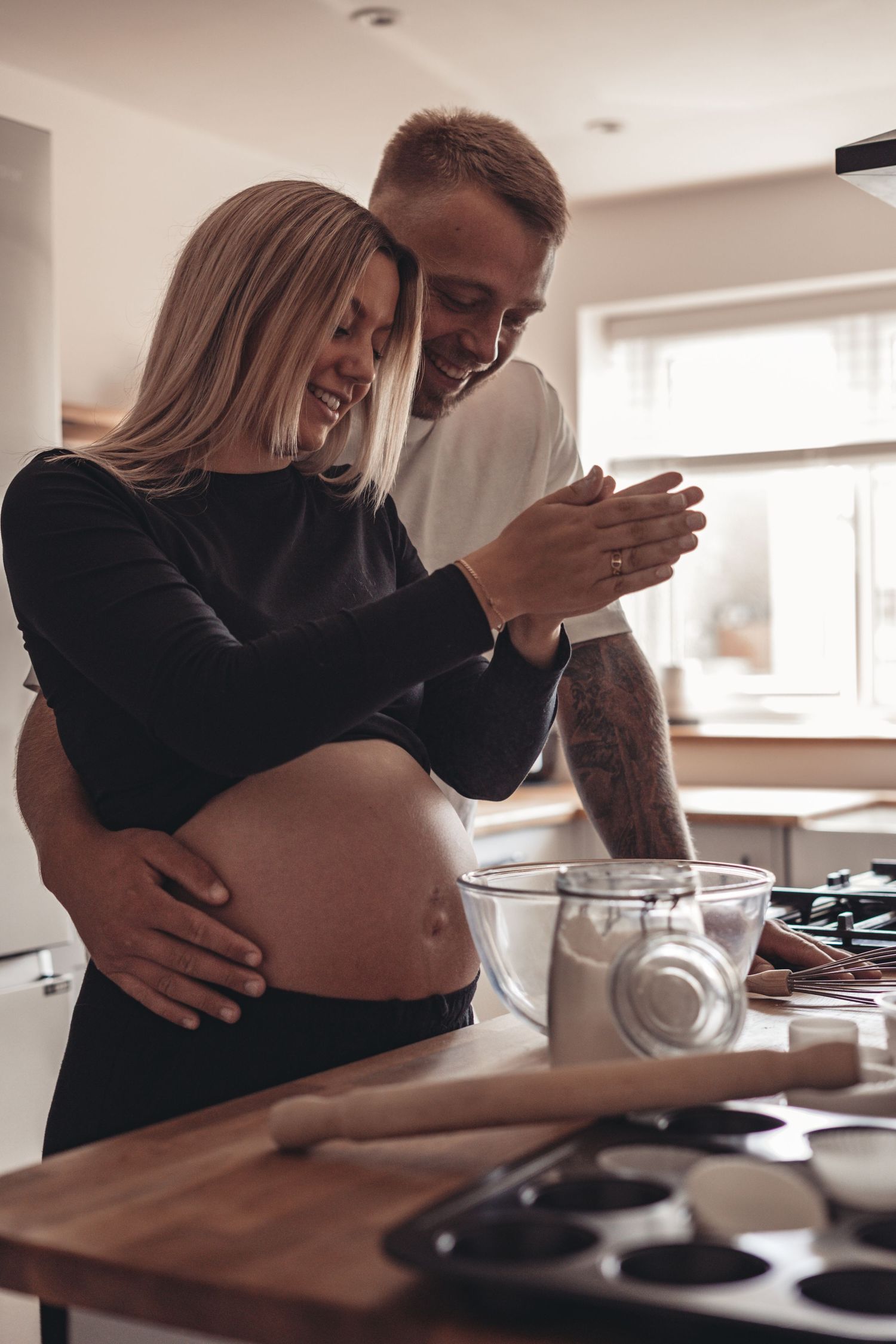 Expecting couple sharing joyful moment while baking in bright kitchen.