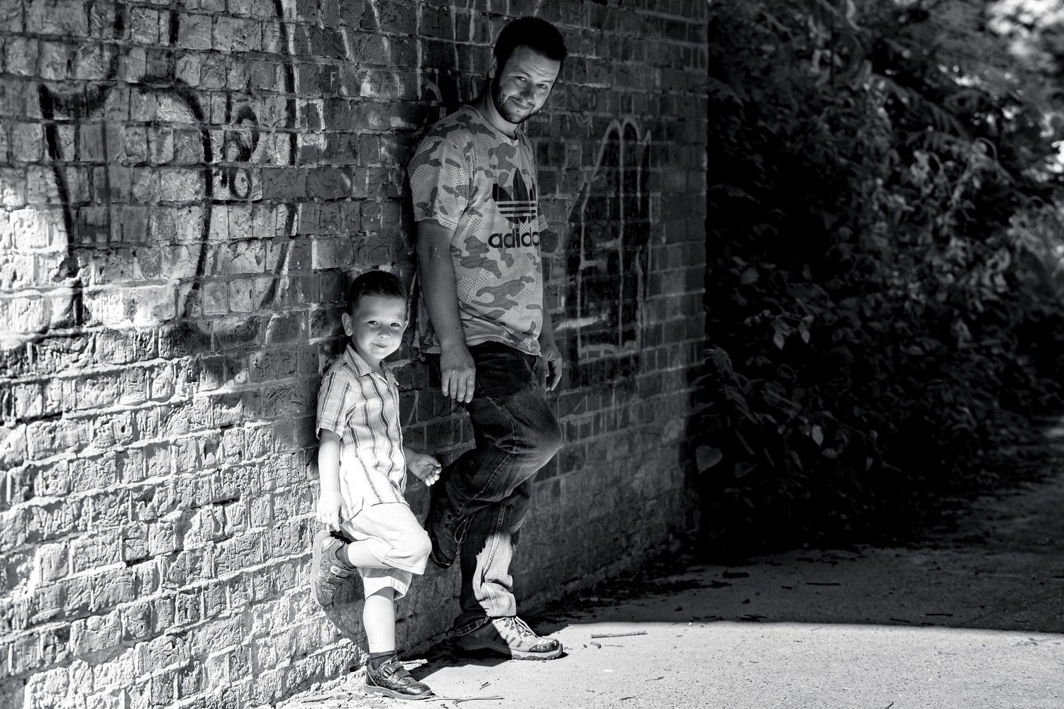 Black and white portrait of two people standing against a brick wall outdoors.