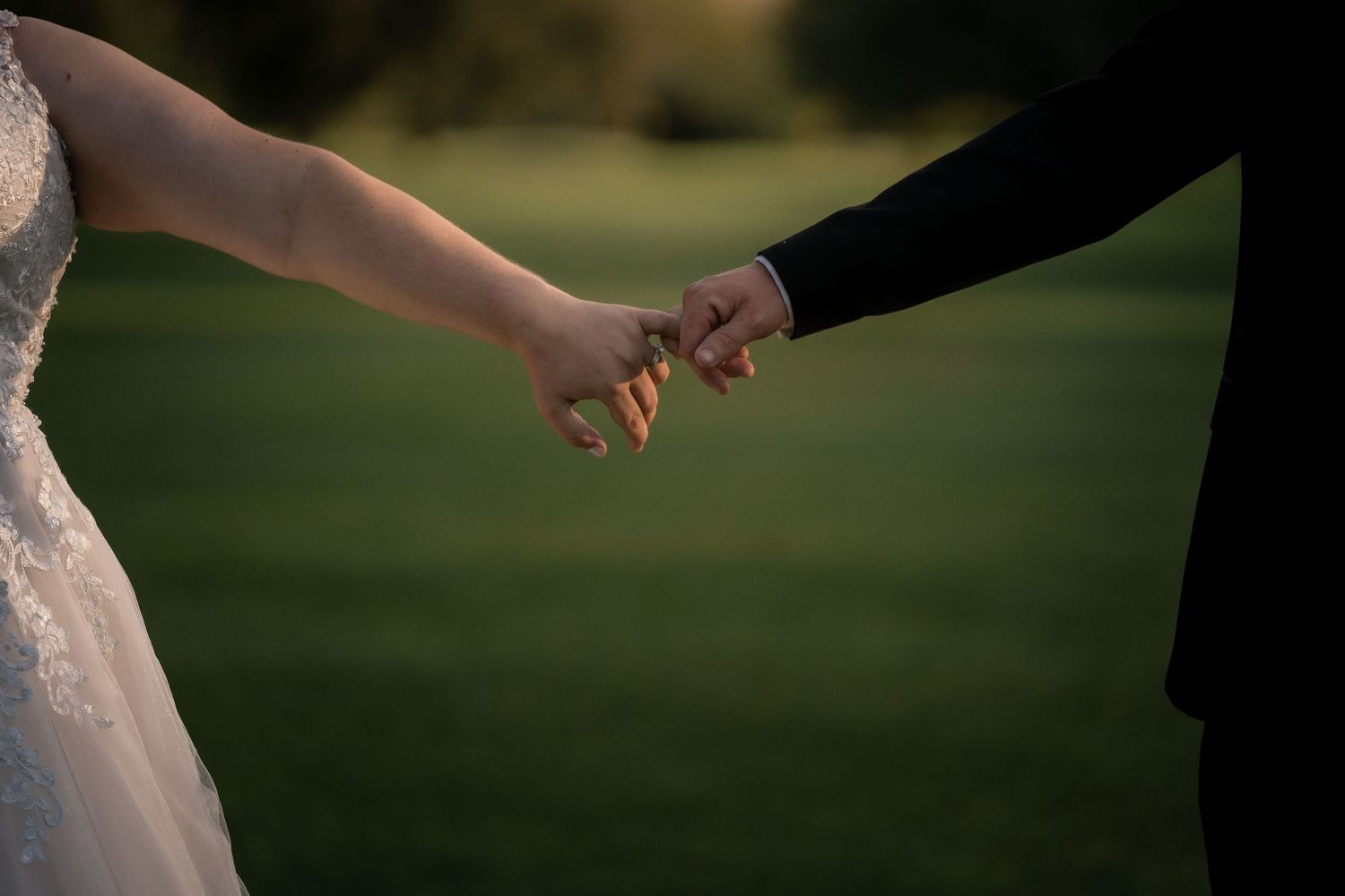 Intimate moment captured of newlyweds holding hands against blurred outdoor background.