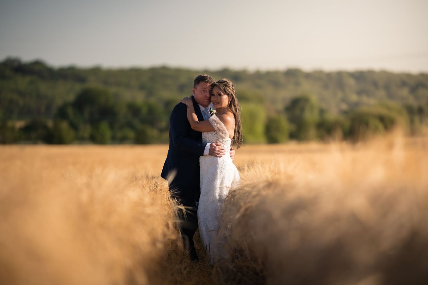 A romantic wedding portrait of a couple embracing in a golden wheat field at sunset.