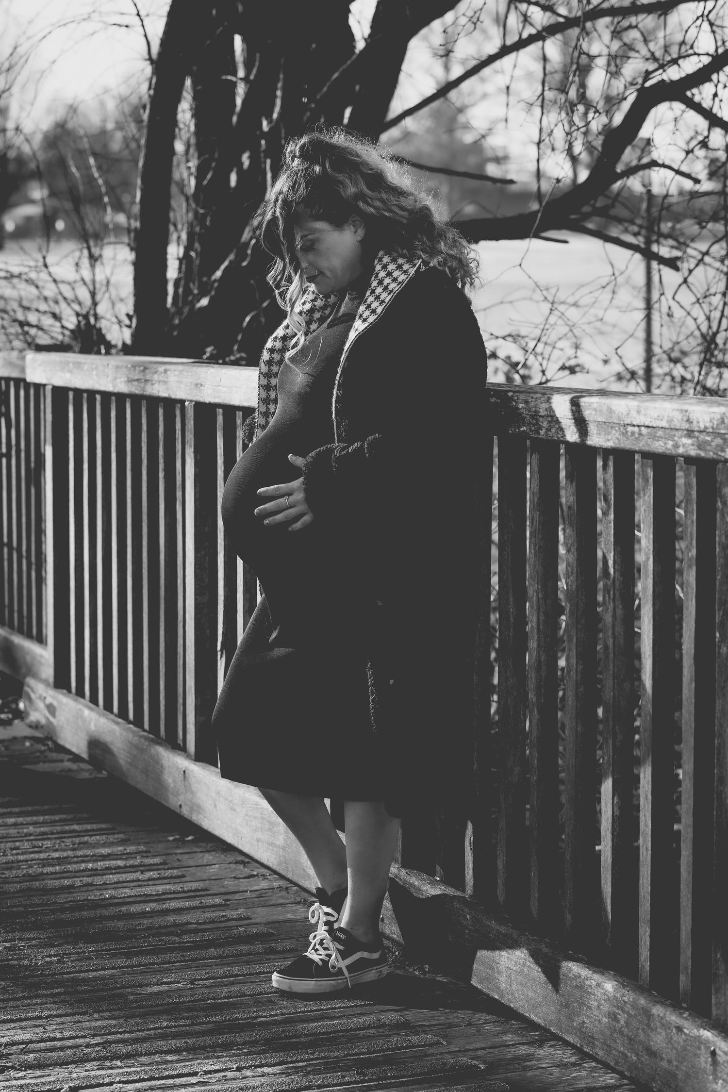 Winter scene of a pregnant woman standing on a wooden bridge in black coat.