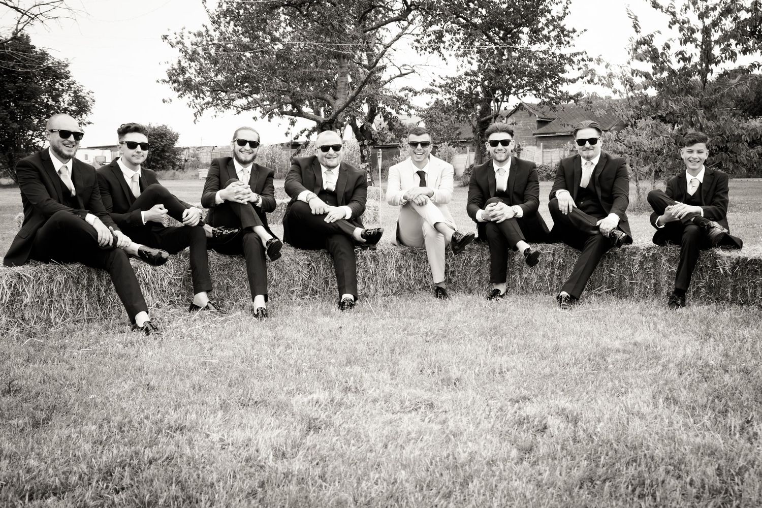 A black and white photo of groomsmen sitting casually on a hillside in formal attire.