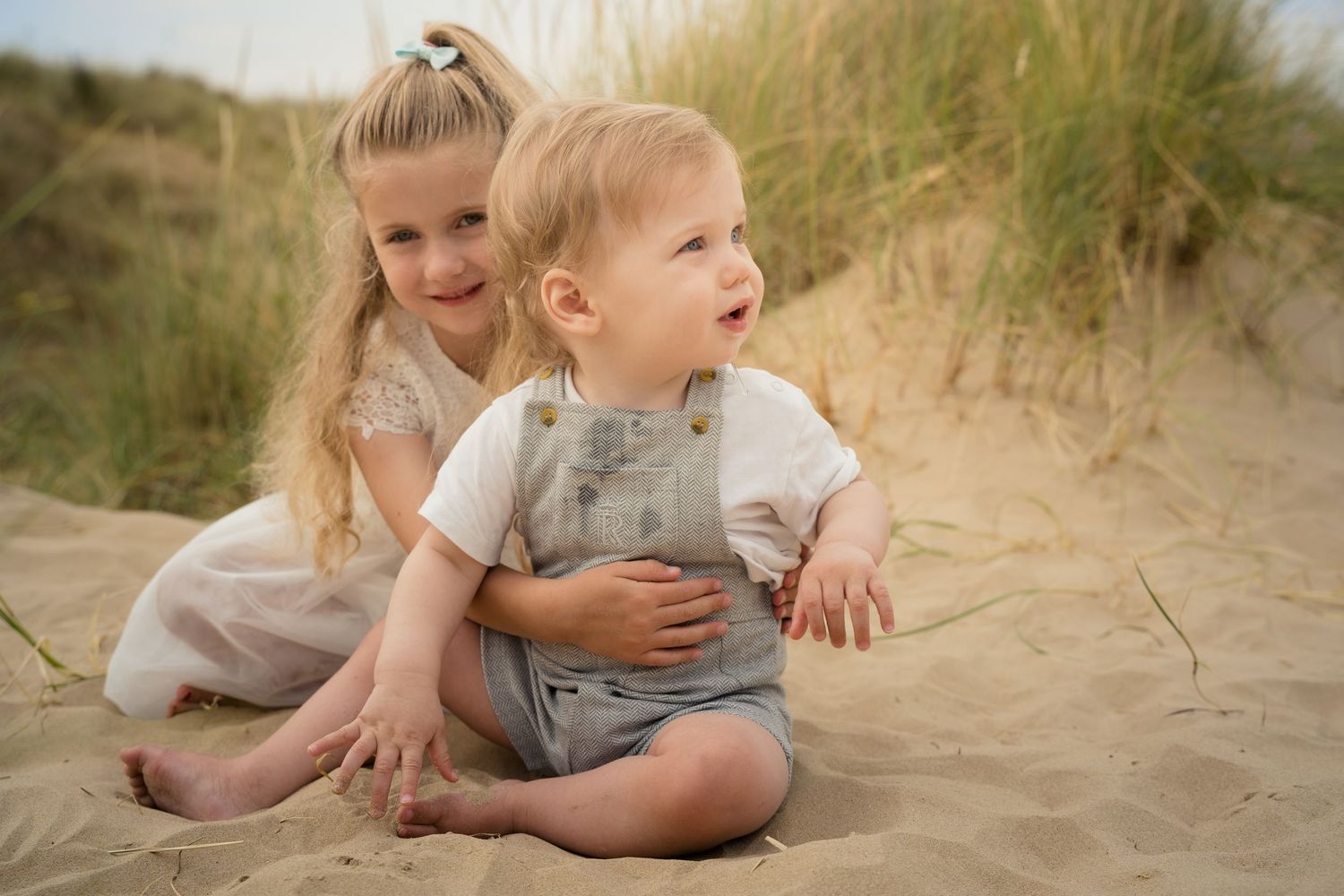 Young children having fun while sitting in beach sand and grass.