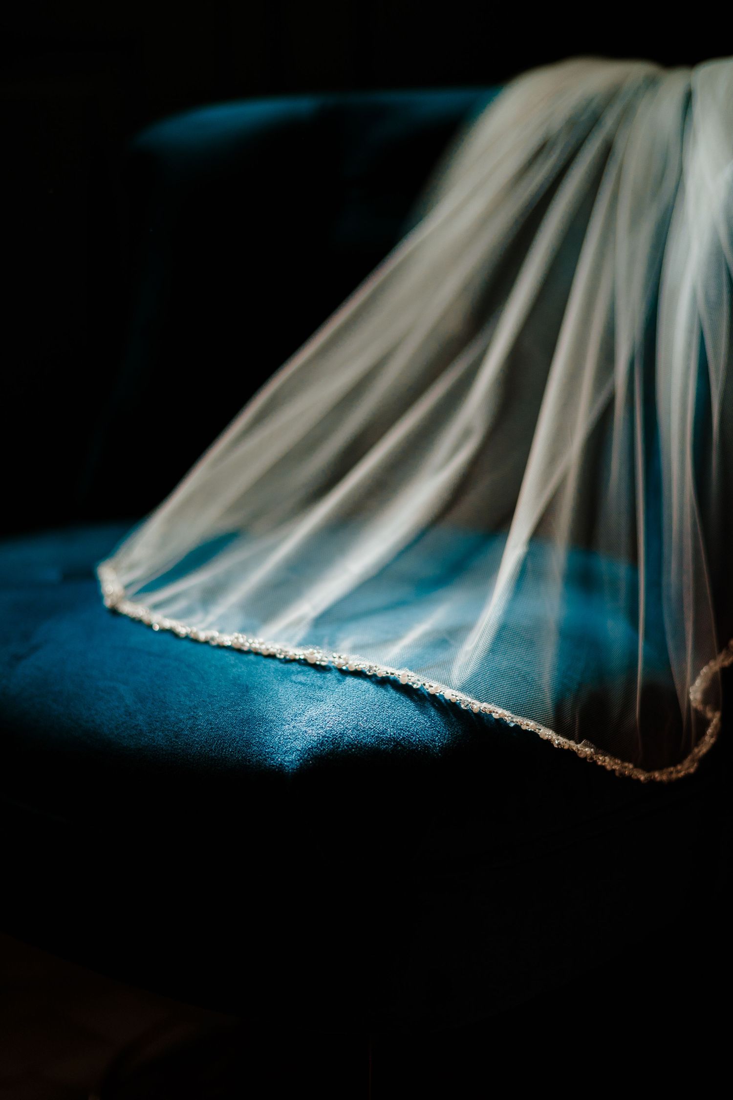 Close-up of delicate white bridal veil with lace trim against dark blue background.