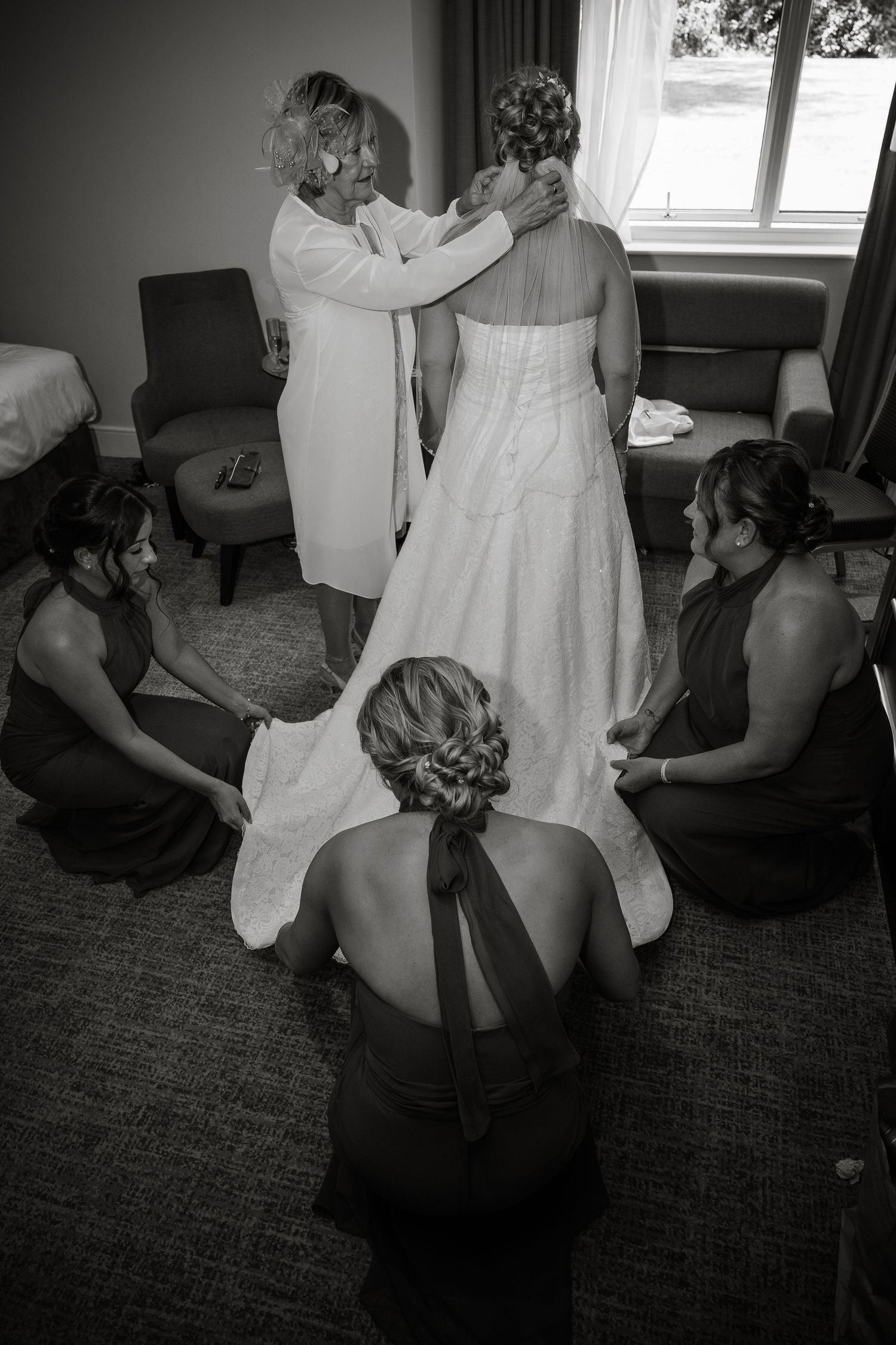 Bridesmaids in dark dresses help adjust a wedding gown during pre-ceremony preparations.