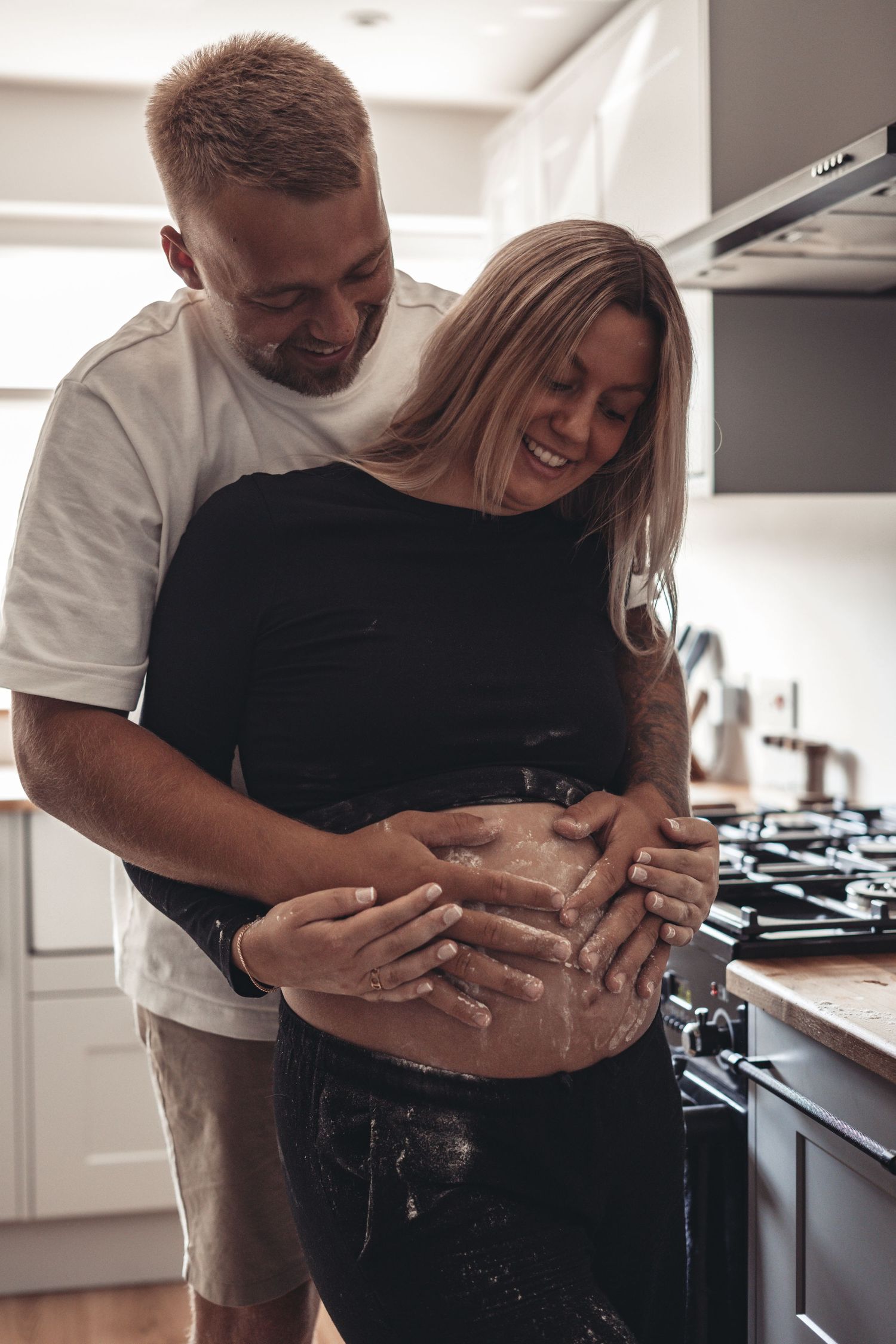 Flour-covered hands embrace pregnant belly during playful kitchen moment.