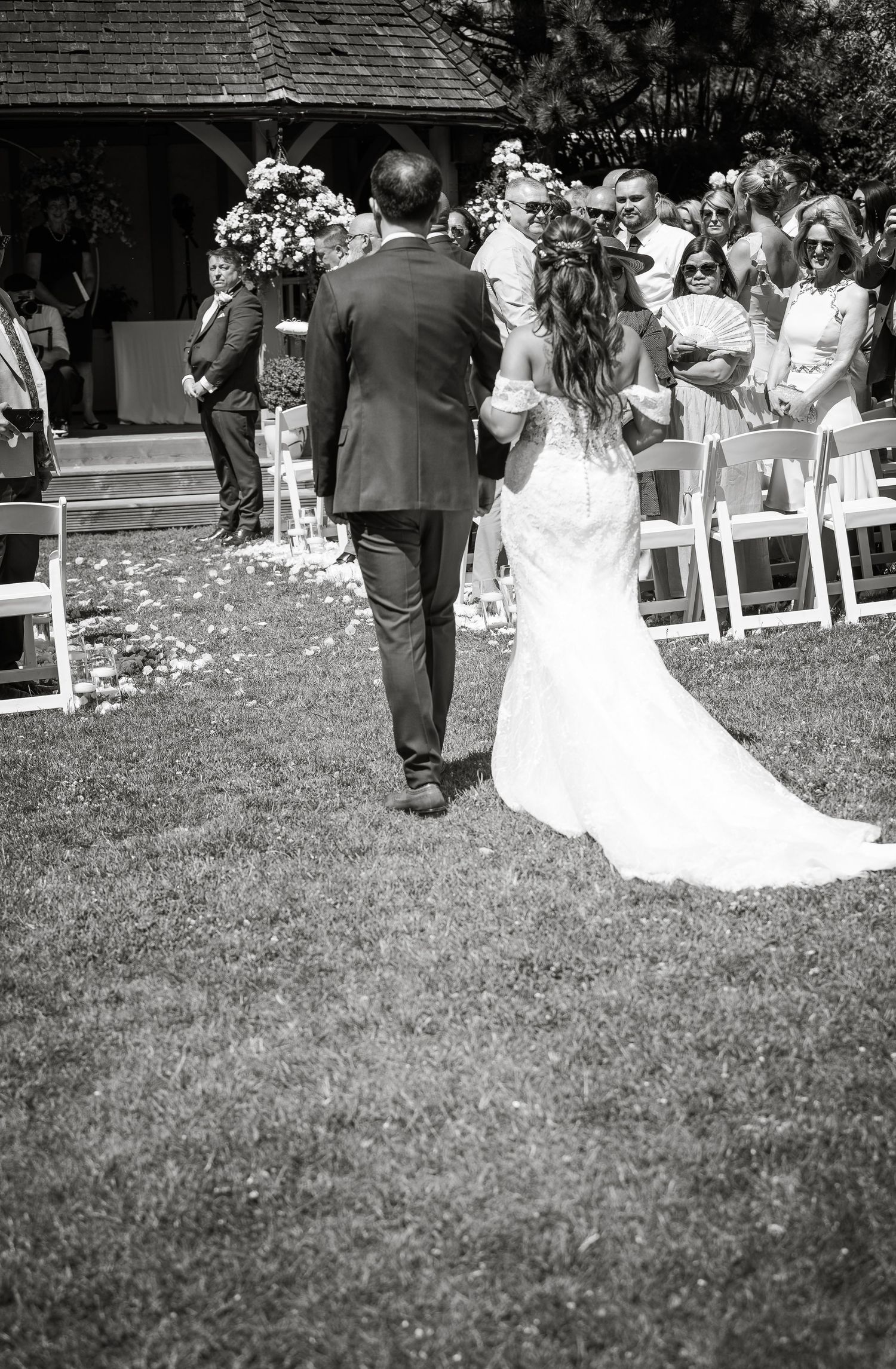 Wedding ceremony guests seated in white chairs on a grassy lawn during an outdoor celebration.