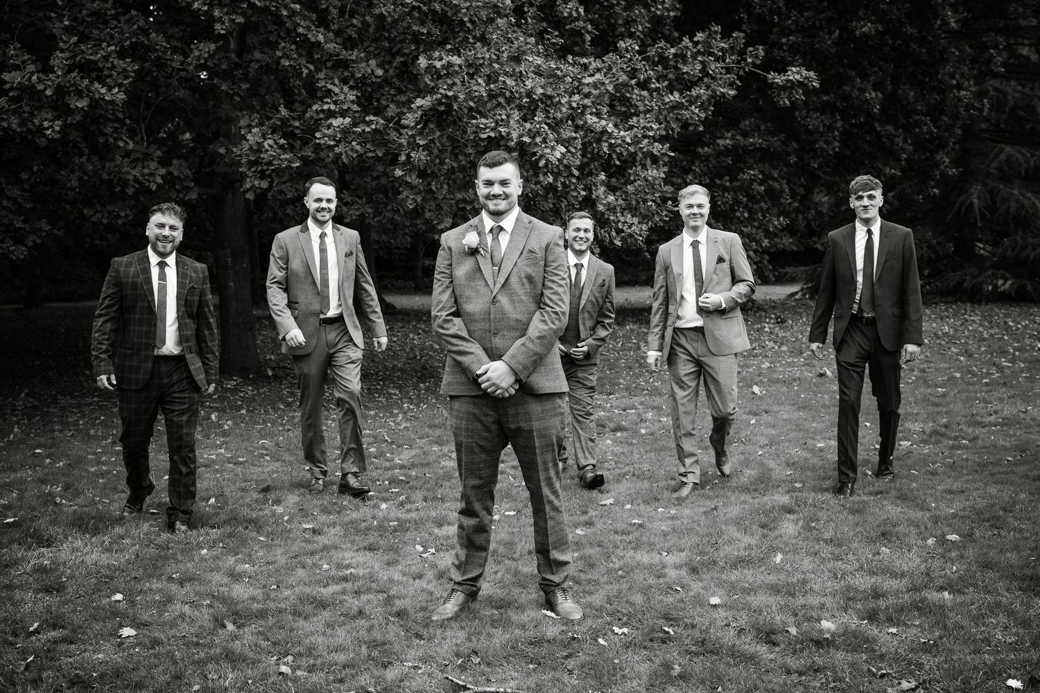A stylish black and white portrait of groomsmen positioned dramatically in a park setting.