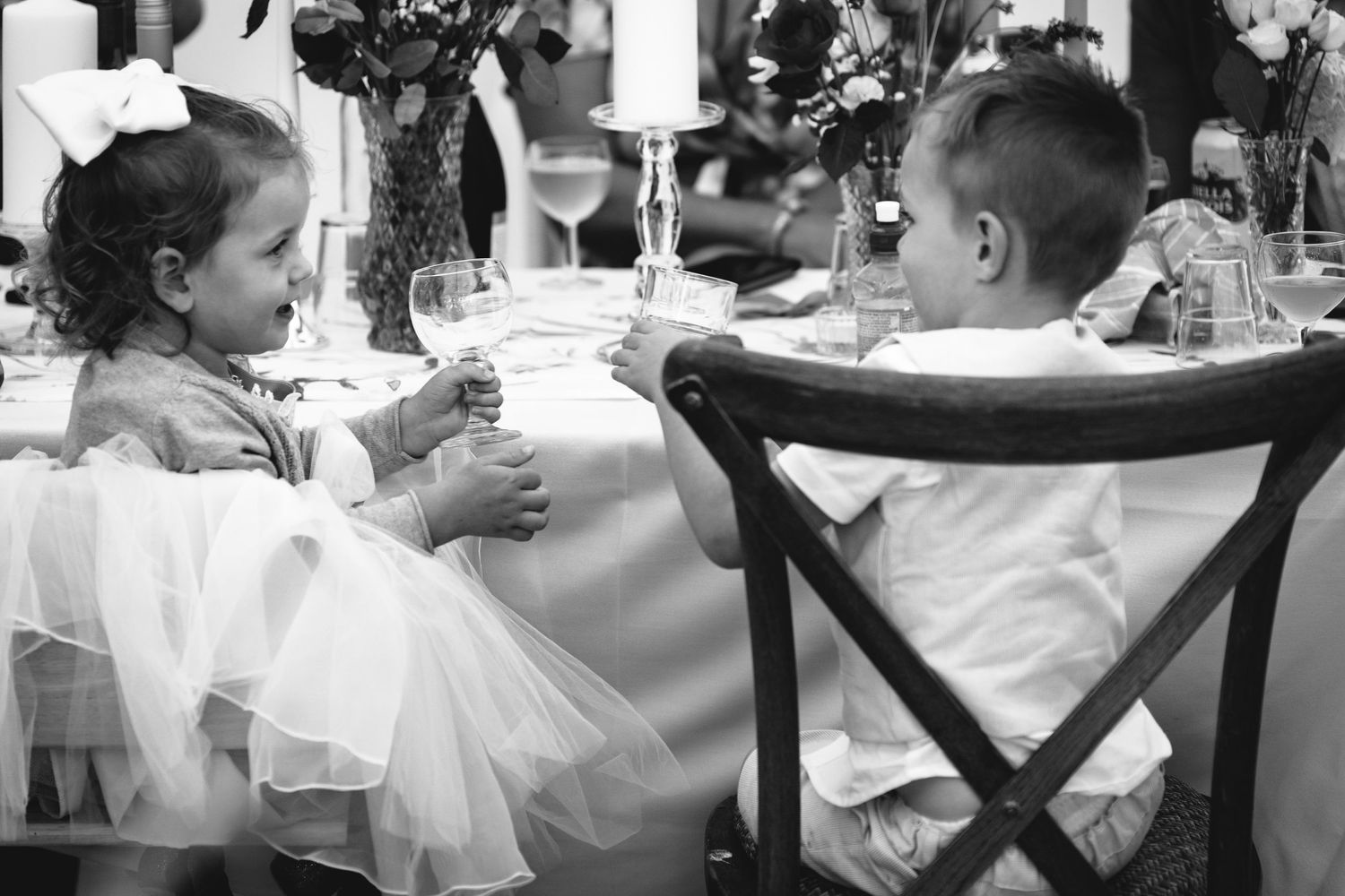 Two children in formal attire sitting at a wedding reception table in black and white.