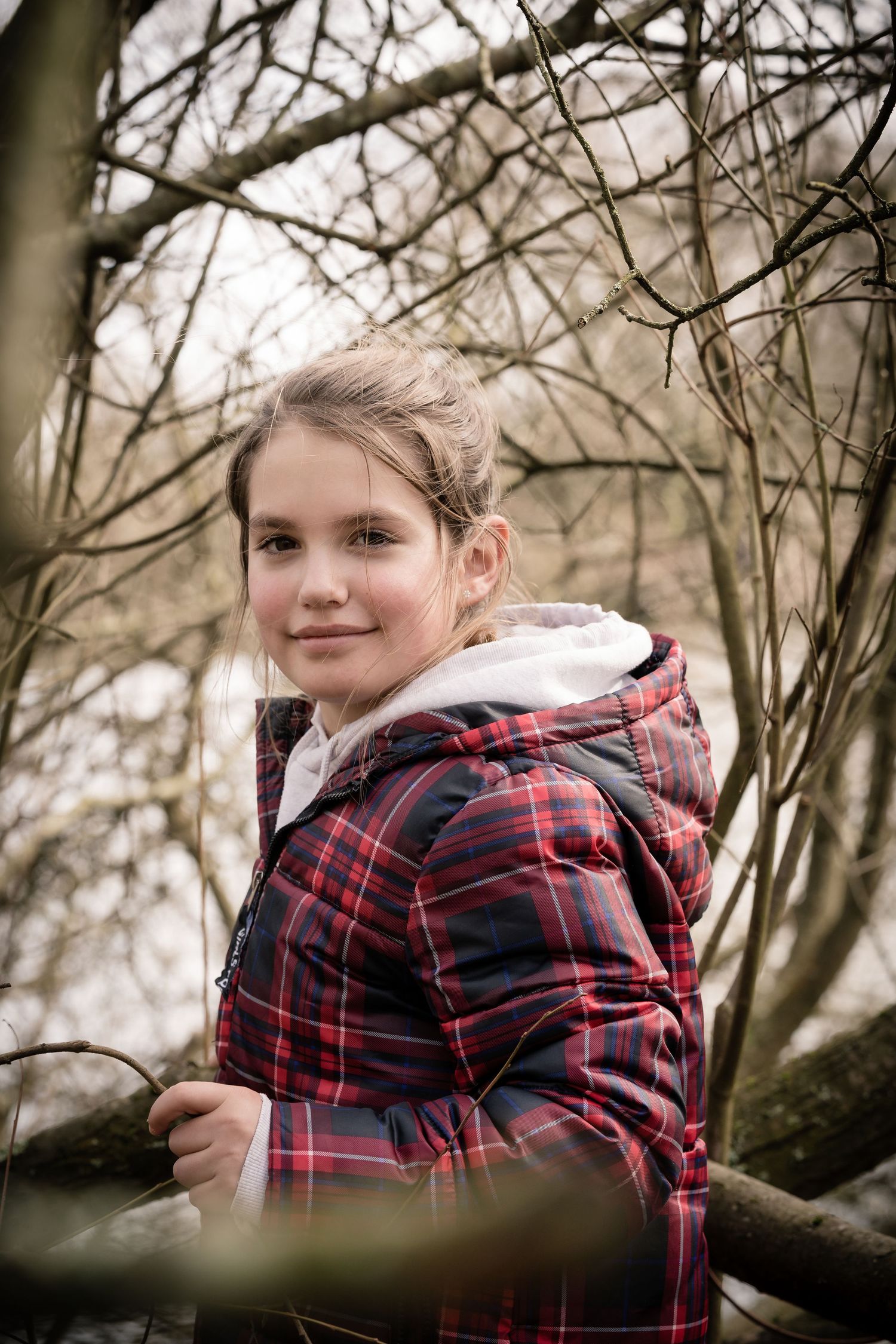 Young person in a plaid winter coat exploring among bare winter branches.