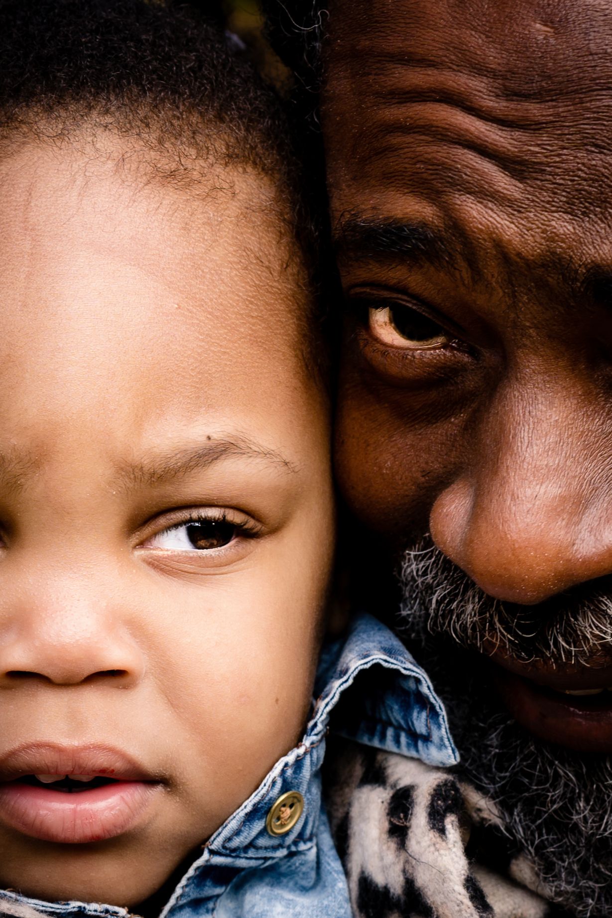 Close up portrait showing two faces in intimate connection against dark background.