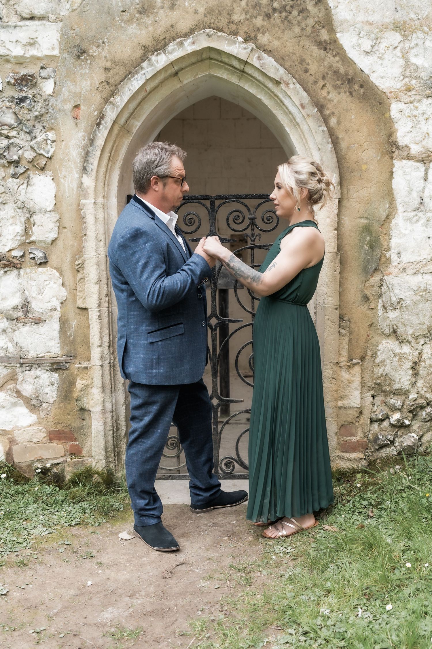A couple in formal attire poses playfully by an ancient stone archway in a series of romantic engagement photos.