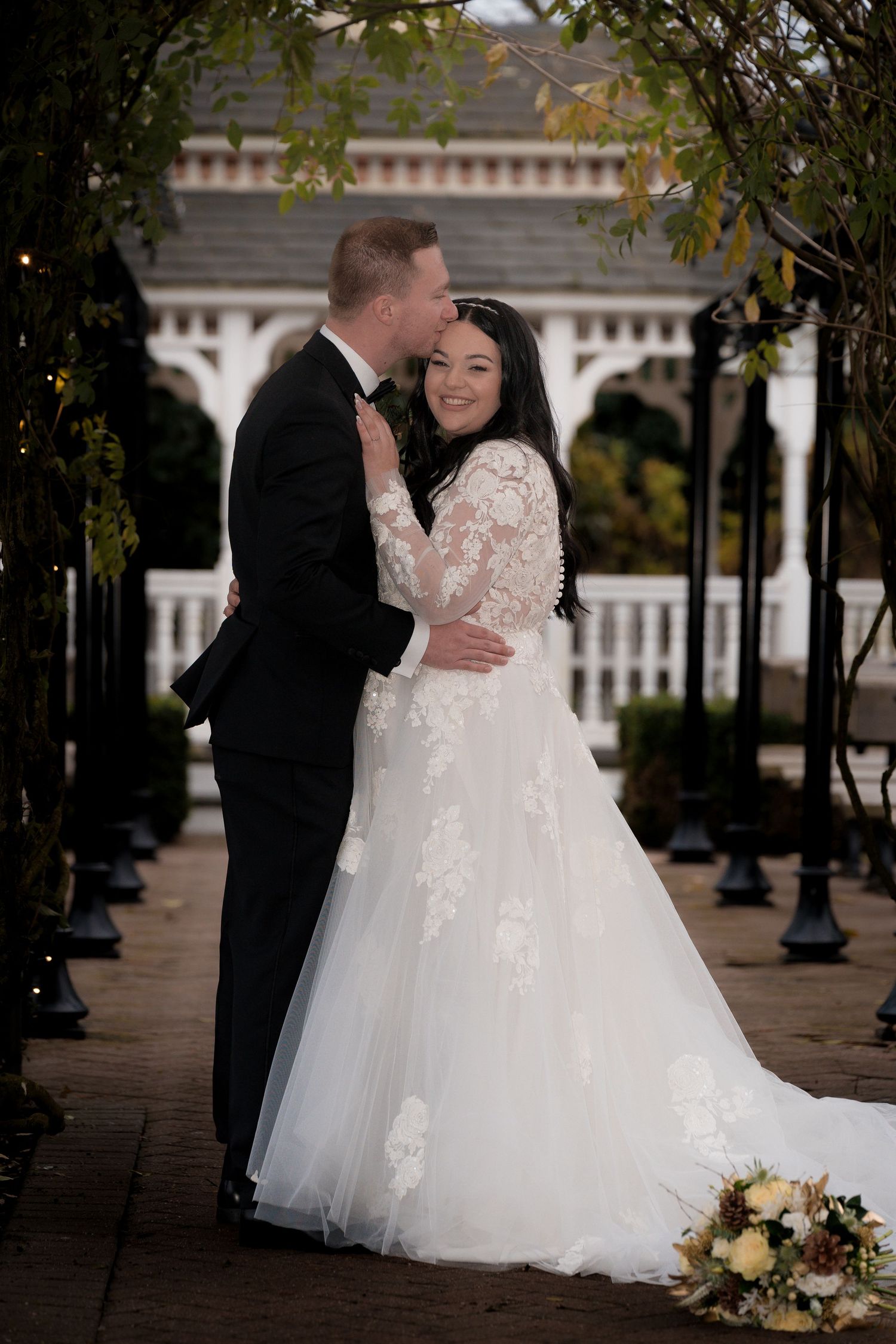 A romantic wedding portrait in front of an elegant white gazebo at dusk.