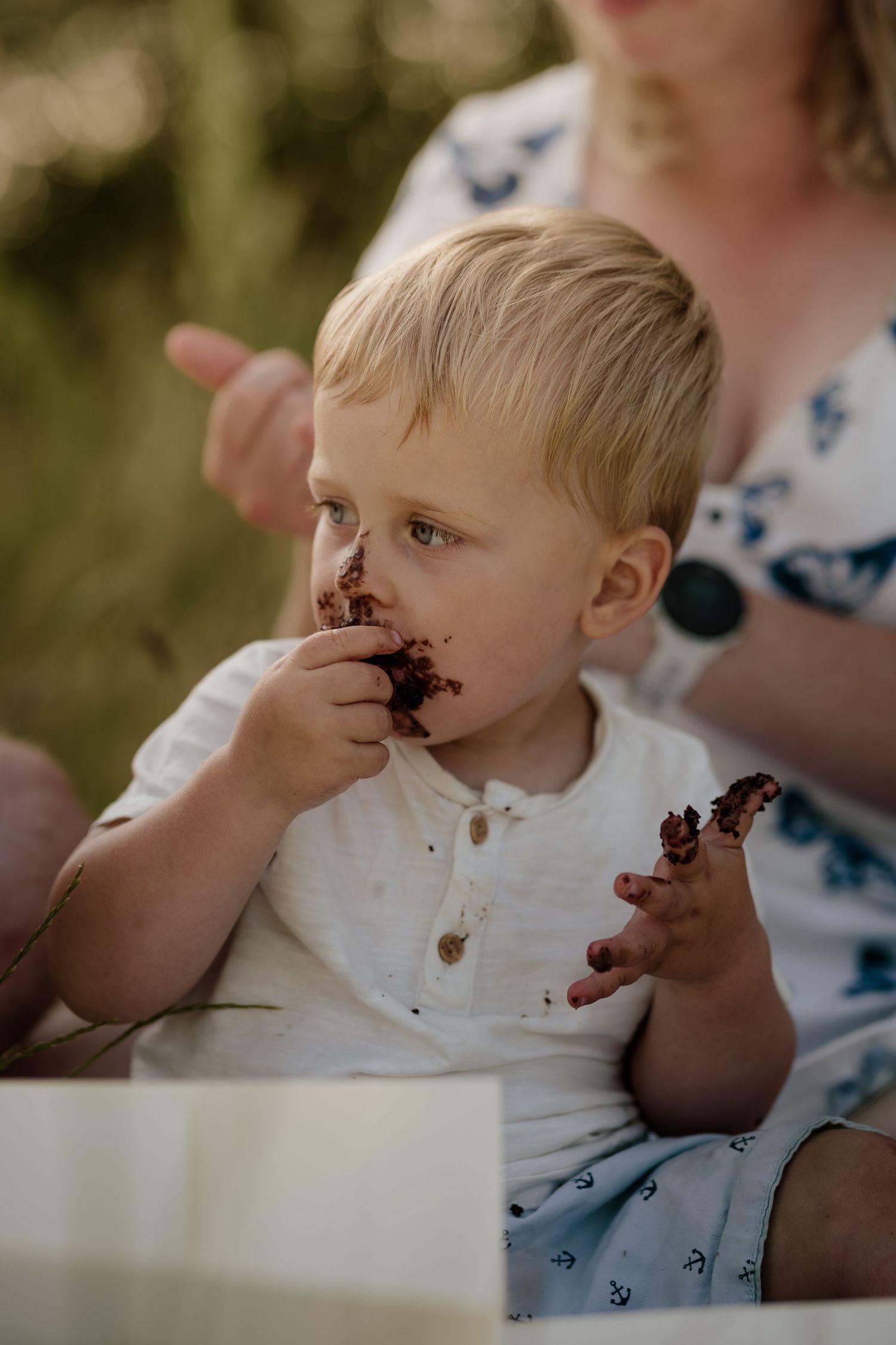 Young child enjoying chocolate cake outdoors on summer day.