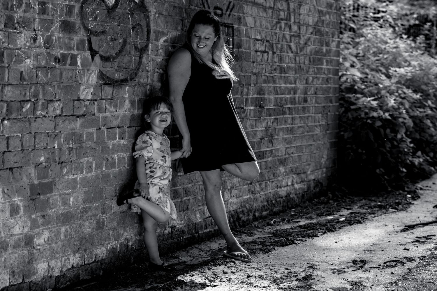 Black and white image of two people leaning against a weathered brick wall.