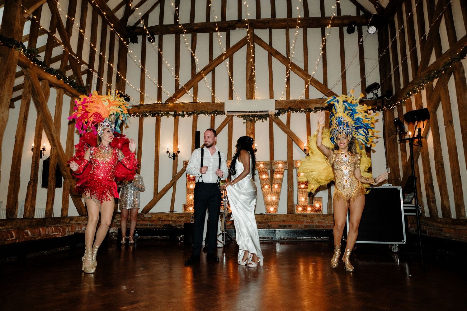A wedding reception scene with performers in colorful costumes in a rustic wooden barn.