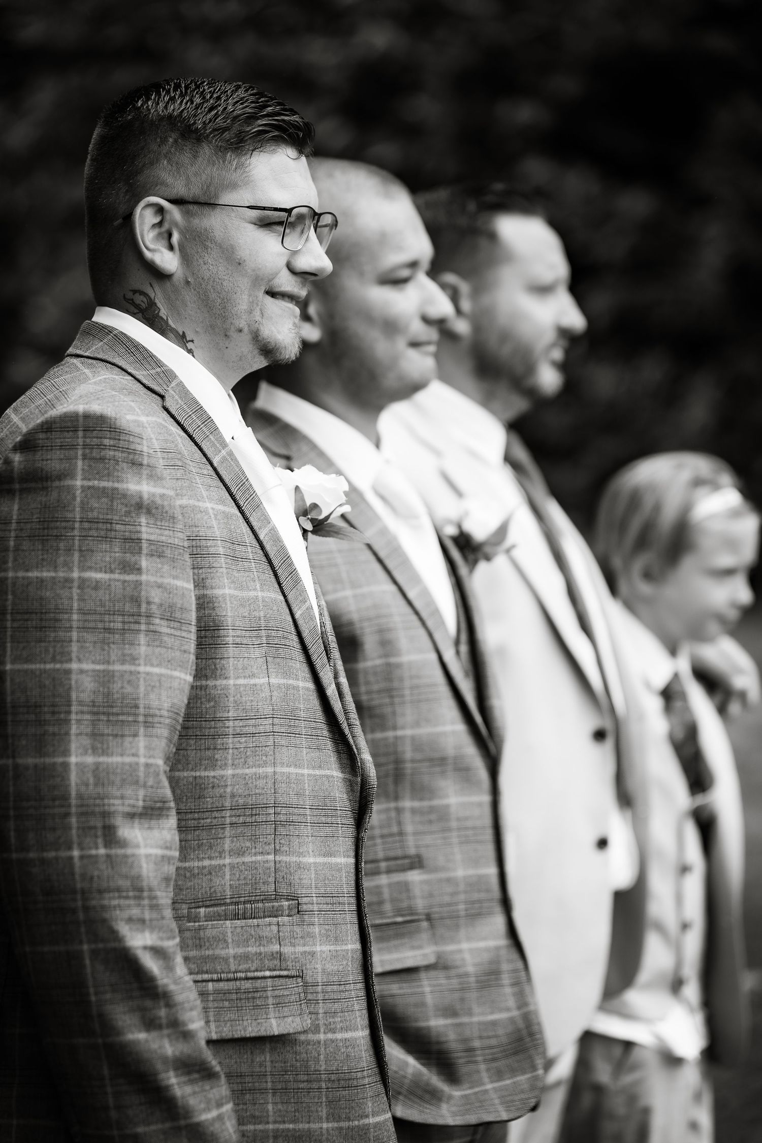 Black and white portrait of wedding party members standing in line wearing formal suits.