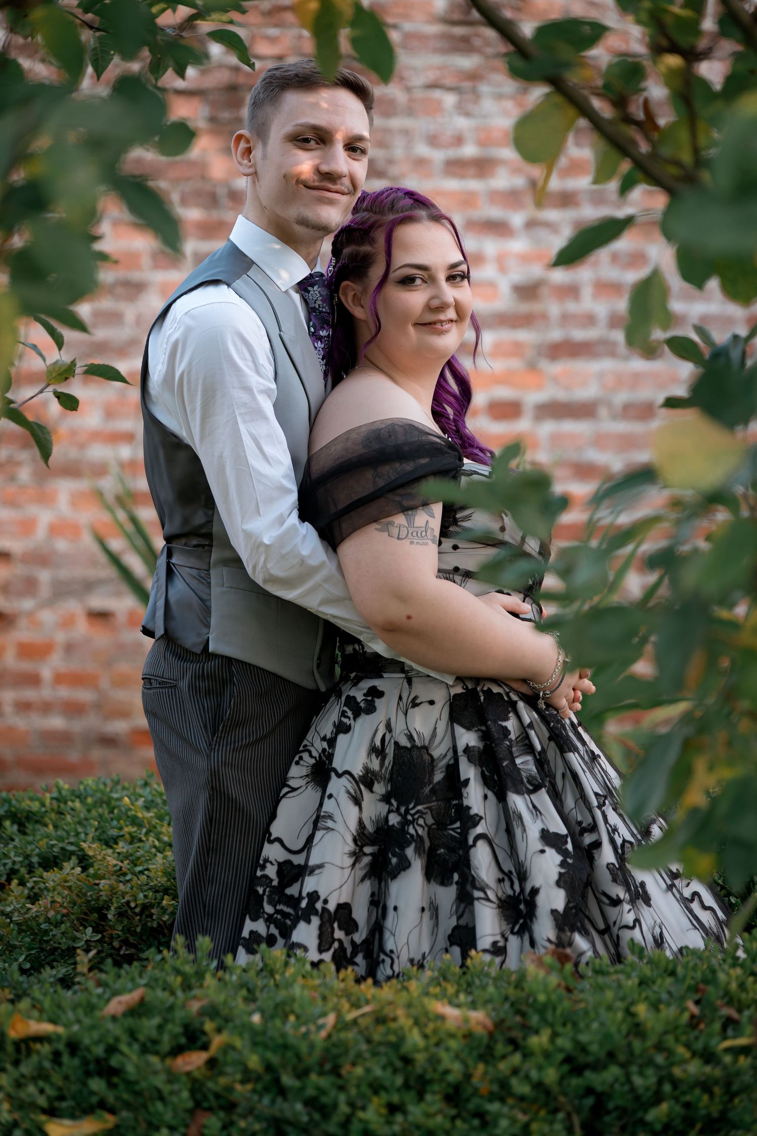 A couple shares a joyful moment in front of a brick wall, with the bride wearing a black and white dress.