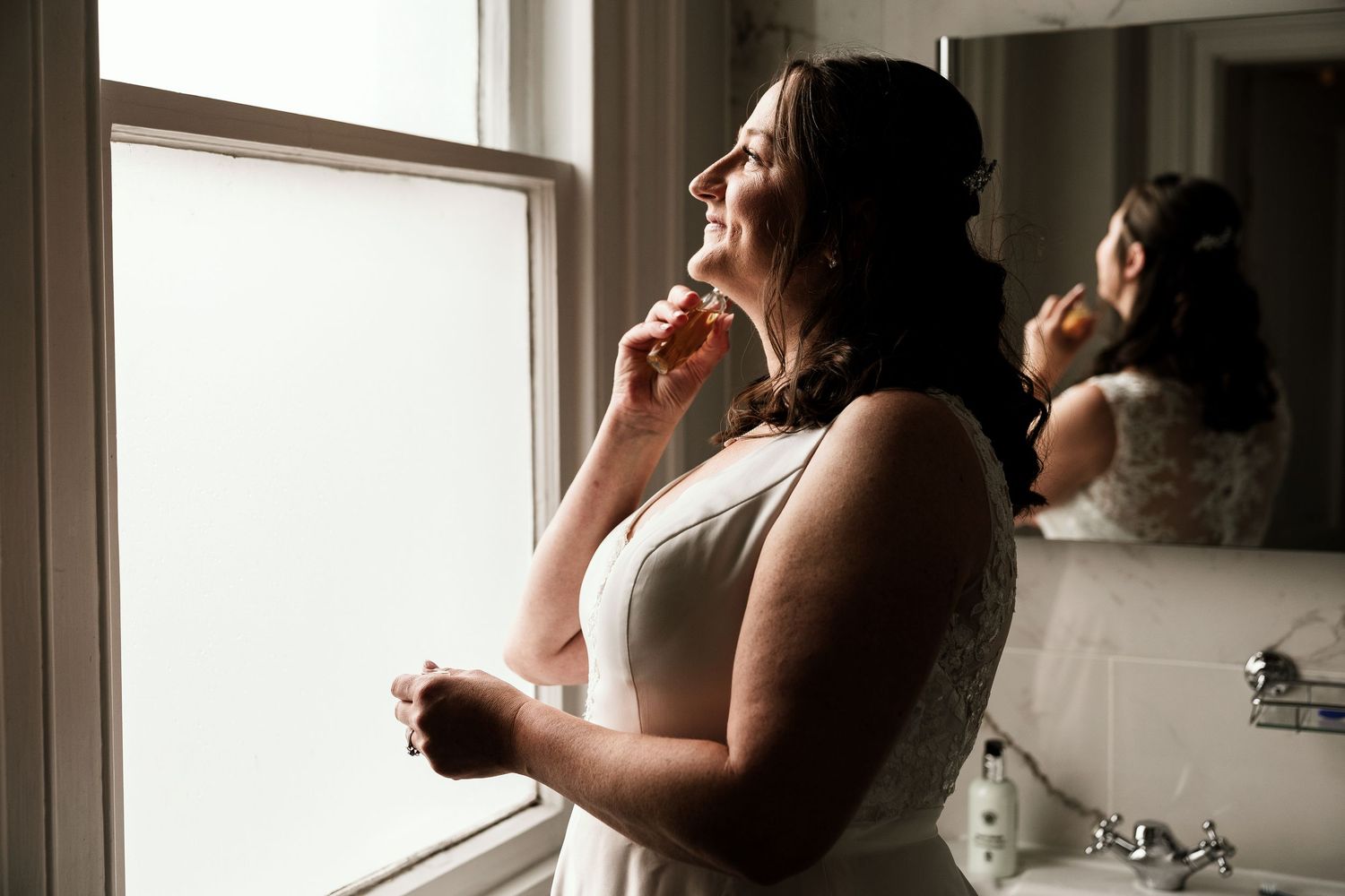 Silhouetted profile of bride getting ready by window in morning light.